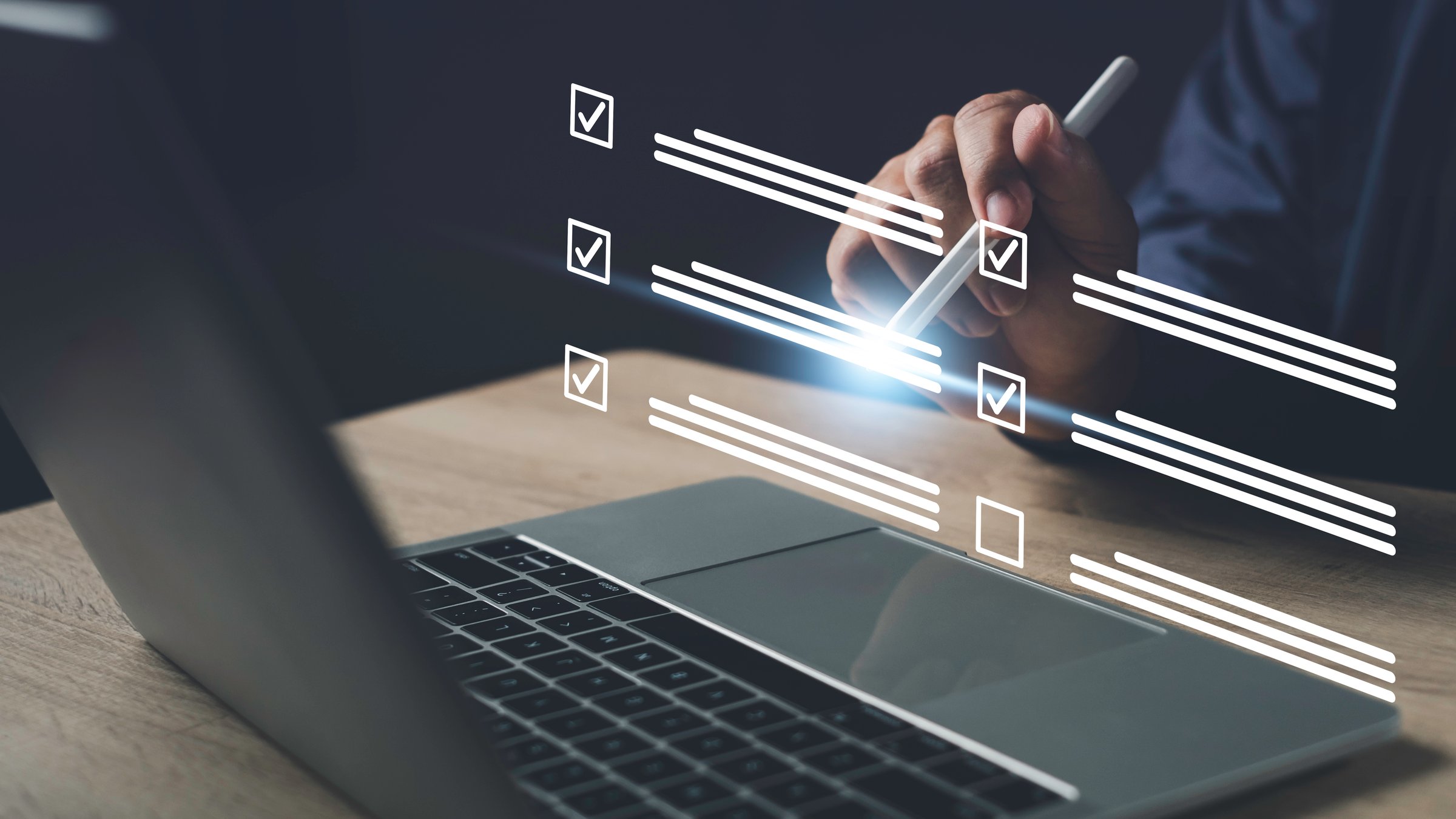 Hand using stylus to fill digital checklist form on laptop screen, representing online survey, task management, and electronic data collection process.