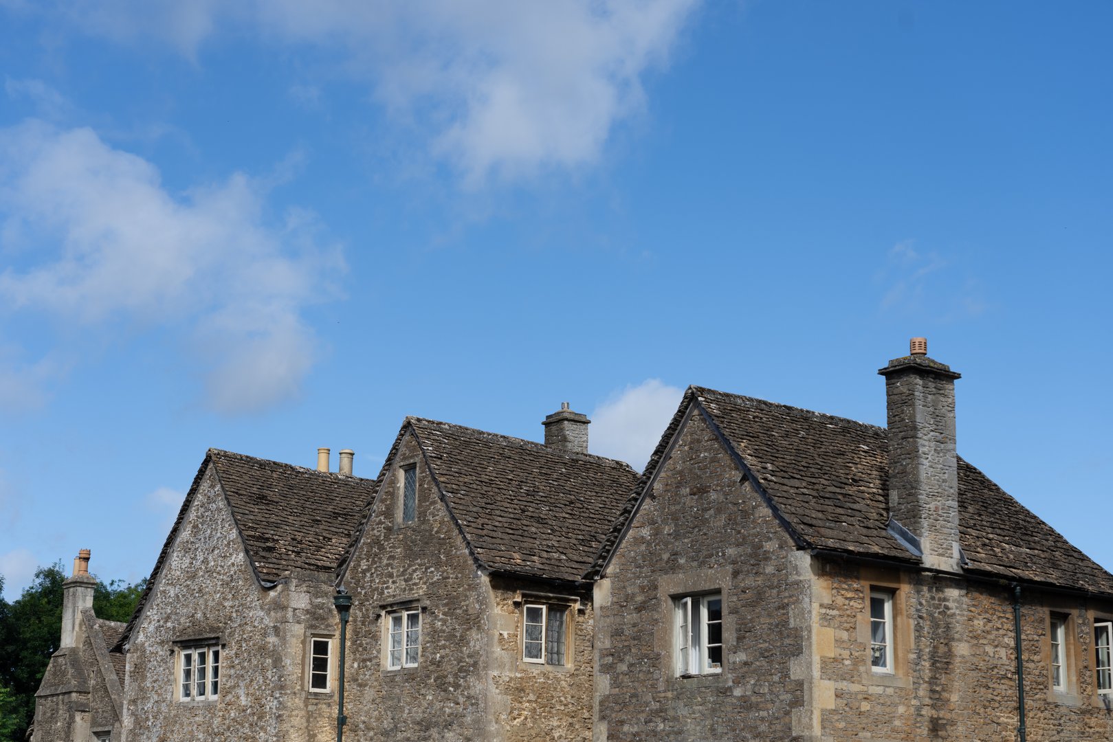 End walls of heritage building homes with row of three gables under blue sky in small town England of Lacock.
