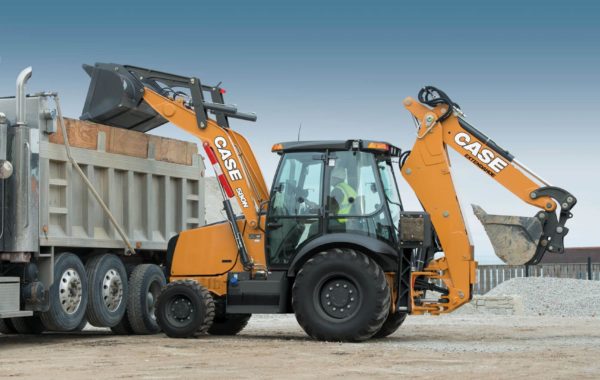 Yellow backhoe loader unloading dirt into a large dump truck at a construction site.