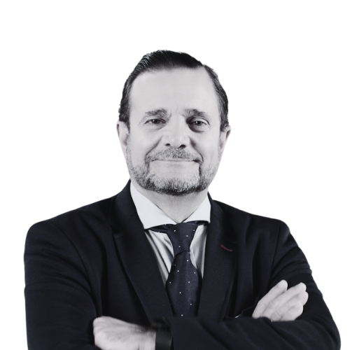 A man in a suit and tie with arms crossed, smiling confidently against a white background.