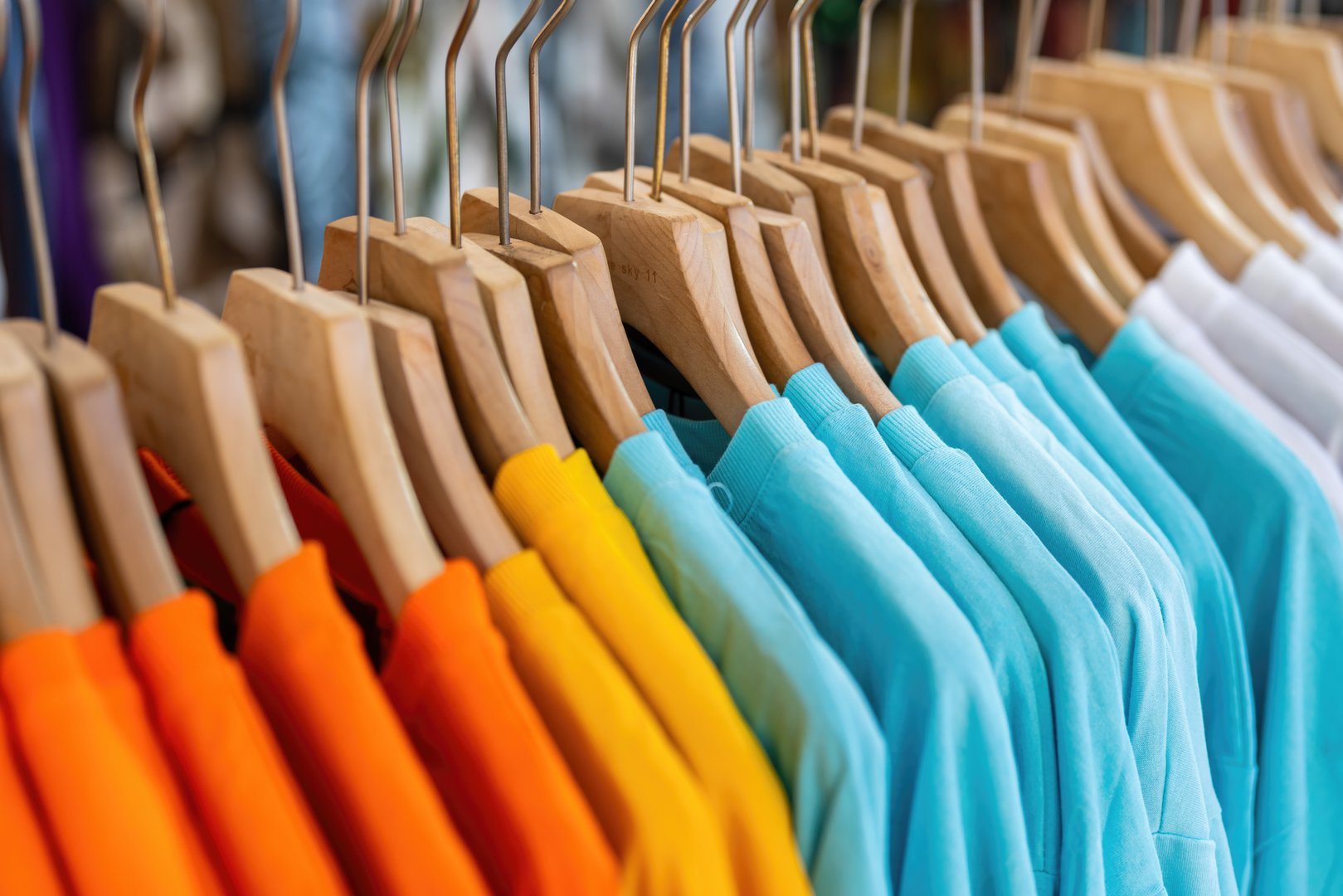 Colorful bright cotton T-Shirt with wooden hanger were hanging on the rack, for sale at modern apparel fashion store.