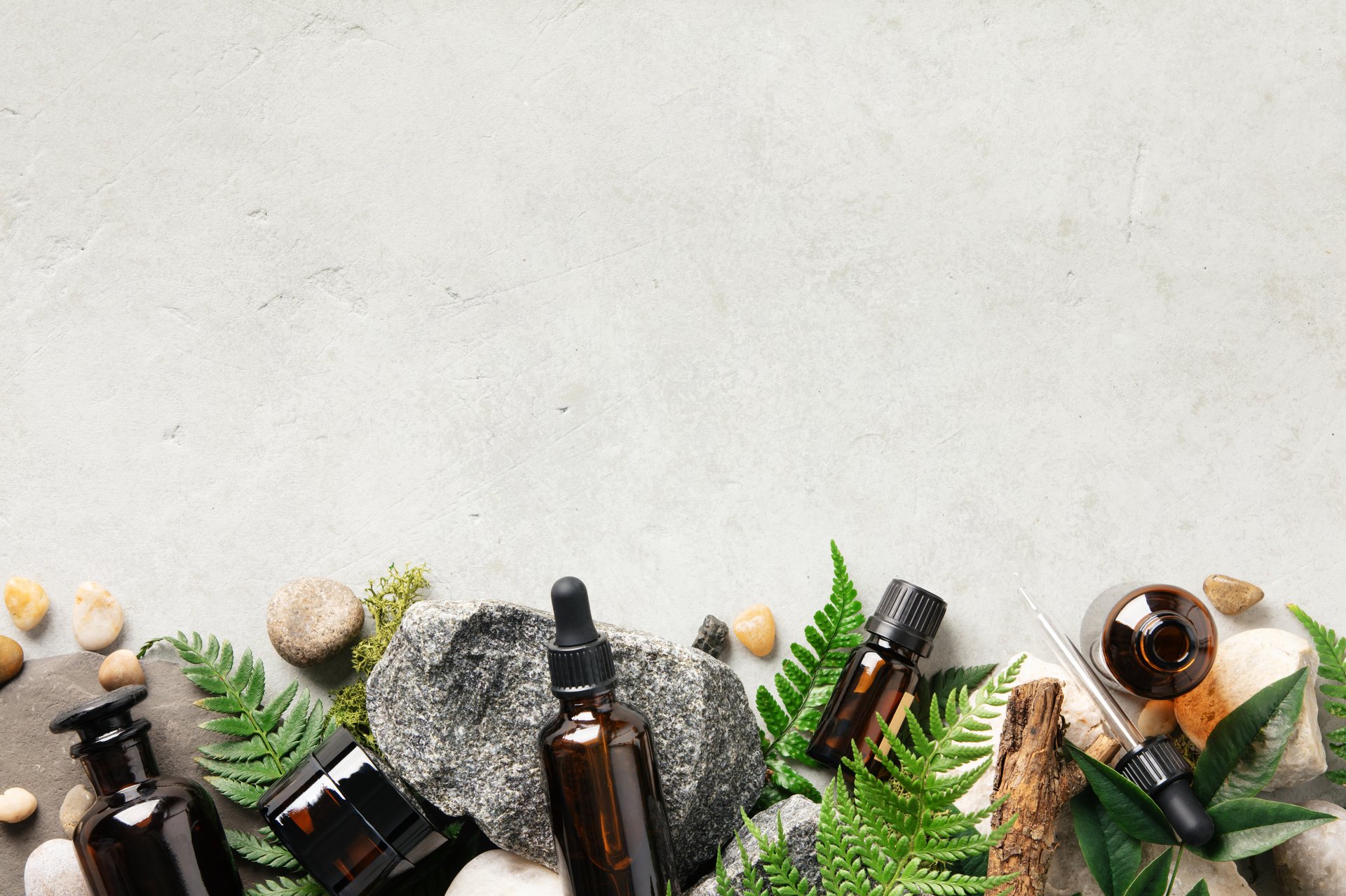 A holistic wellness arrangement featuring essential oil bottles, rocks, and green leaves for a spa or natural product theme.