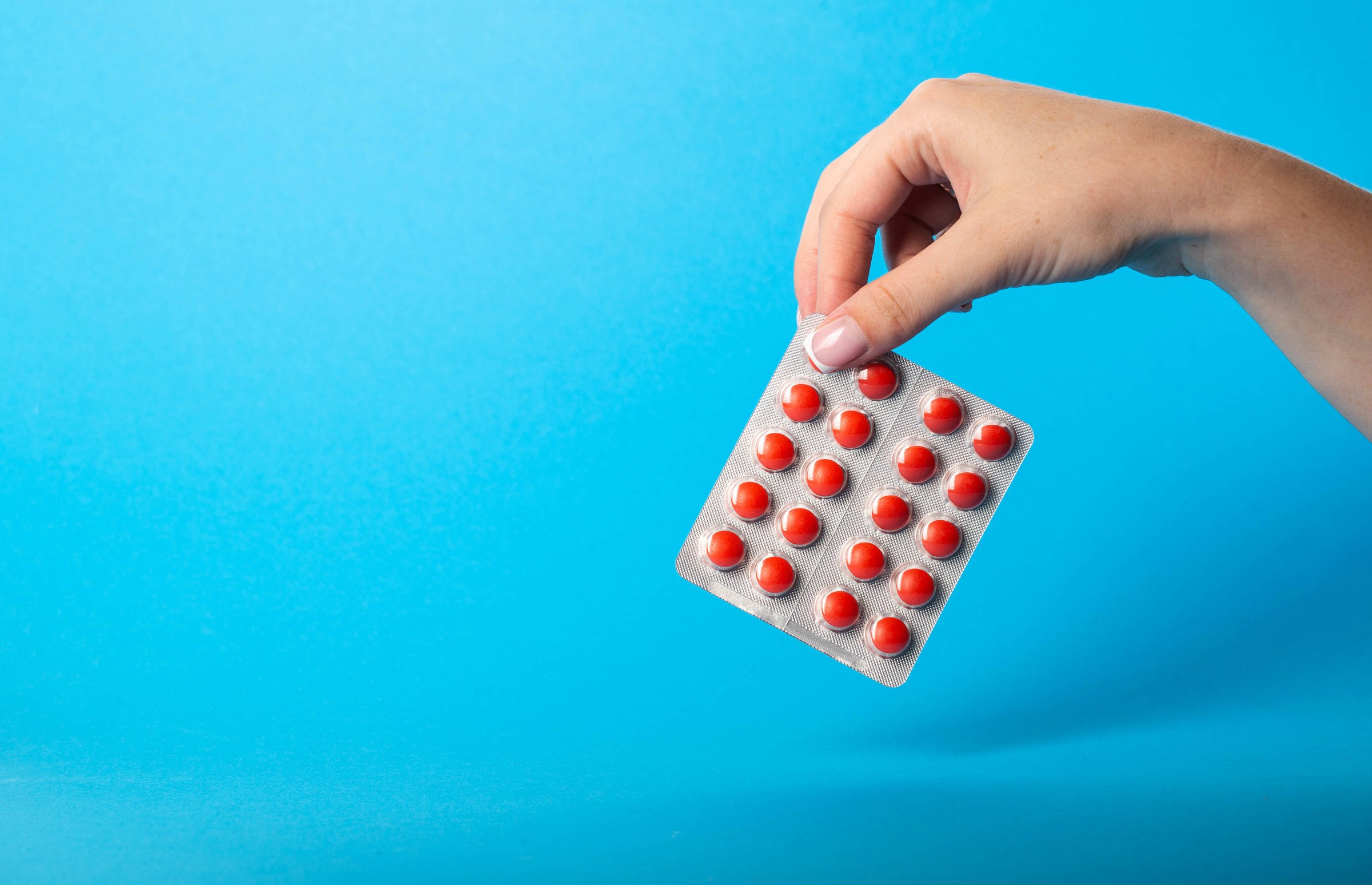 Female hand holding blisters with red pills on blue background. Concept of sedatives in pharmaceuticals. Sedatives and calming drugs