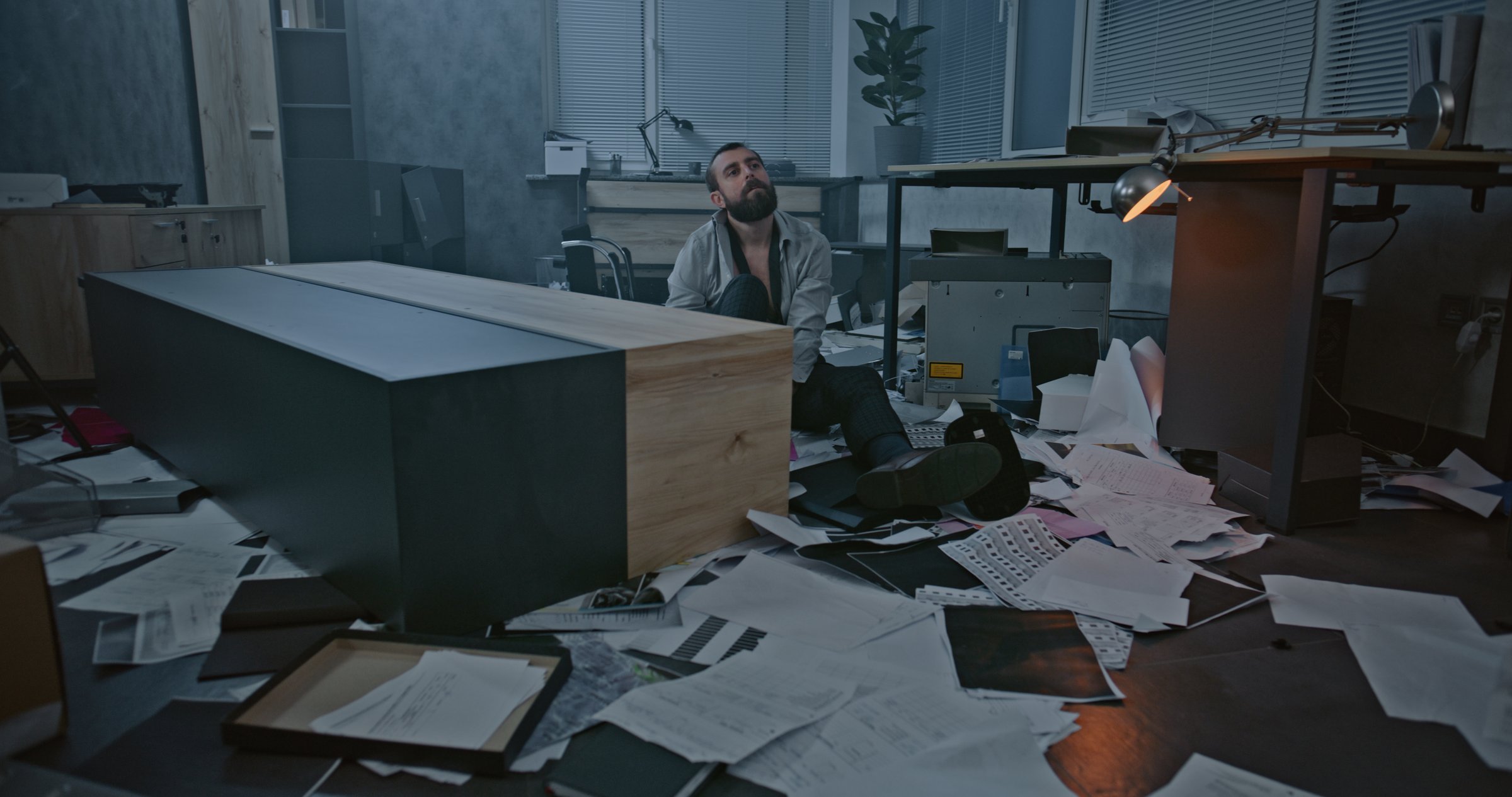 Dolly shot of depressed office worker sitting on the floor in destroyed office room. Frustrated businessman after fit of rage over unsuccessful business deal or receiving bad news. Burnout at work.