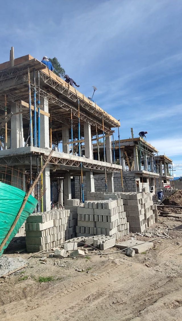 Construction site with workers building a multi-story structure using concrete blocks and scaffolding under a blue sky.