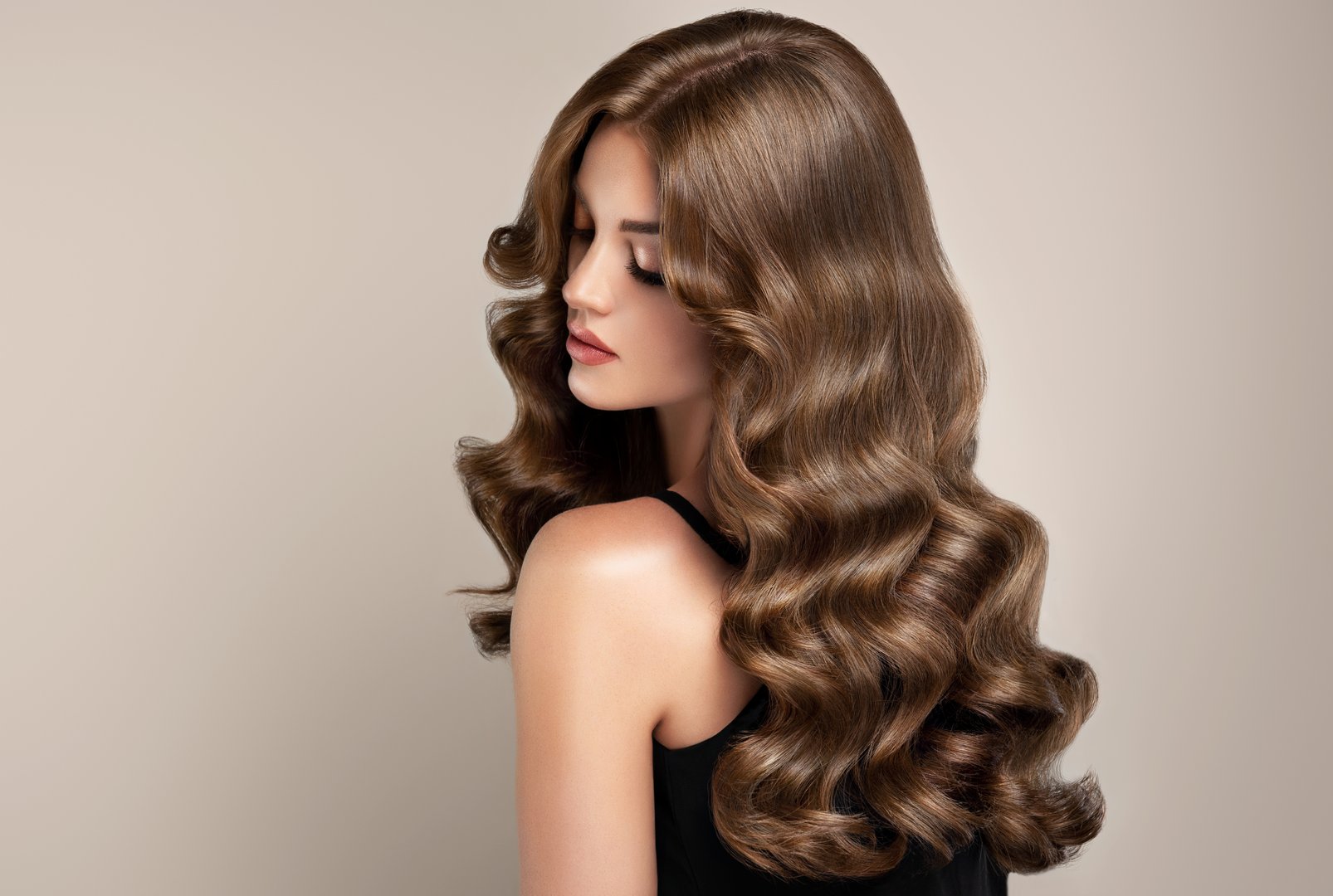 Portrait of brunette with elegant wavy long hairstyle. Brown haired pretty woman is demonstrating perfect dense waves of healthy well cared long hair. Hairdressing art  hair care and makeup.