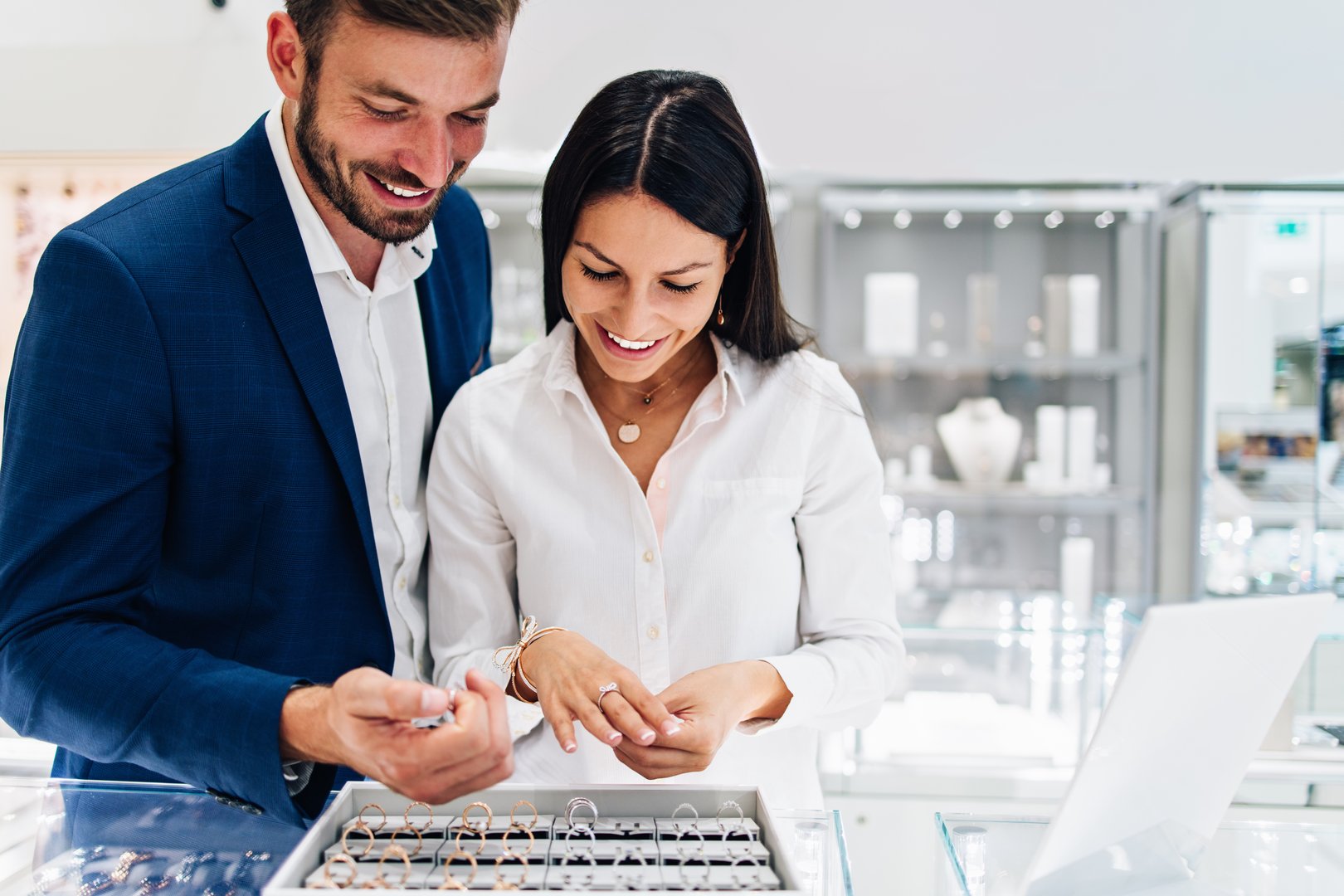 Beautiful couple enjoying in shopping at modern jewelry store. Young woman try it out gorgeous necklace and ring.
