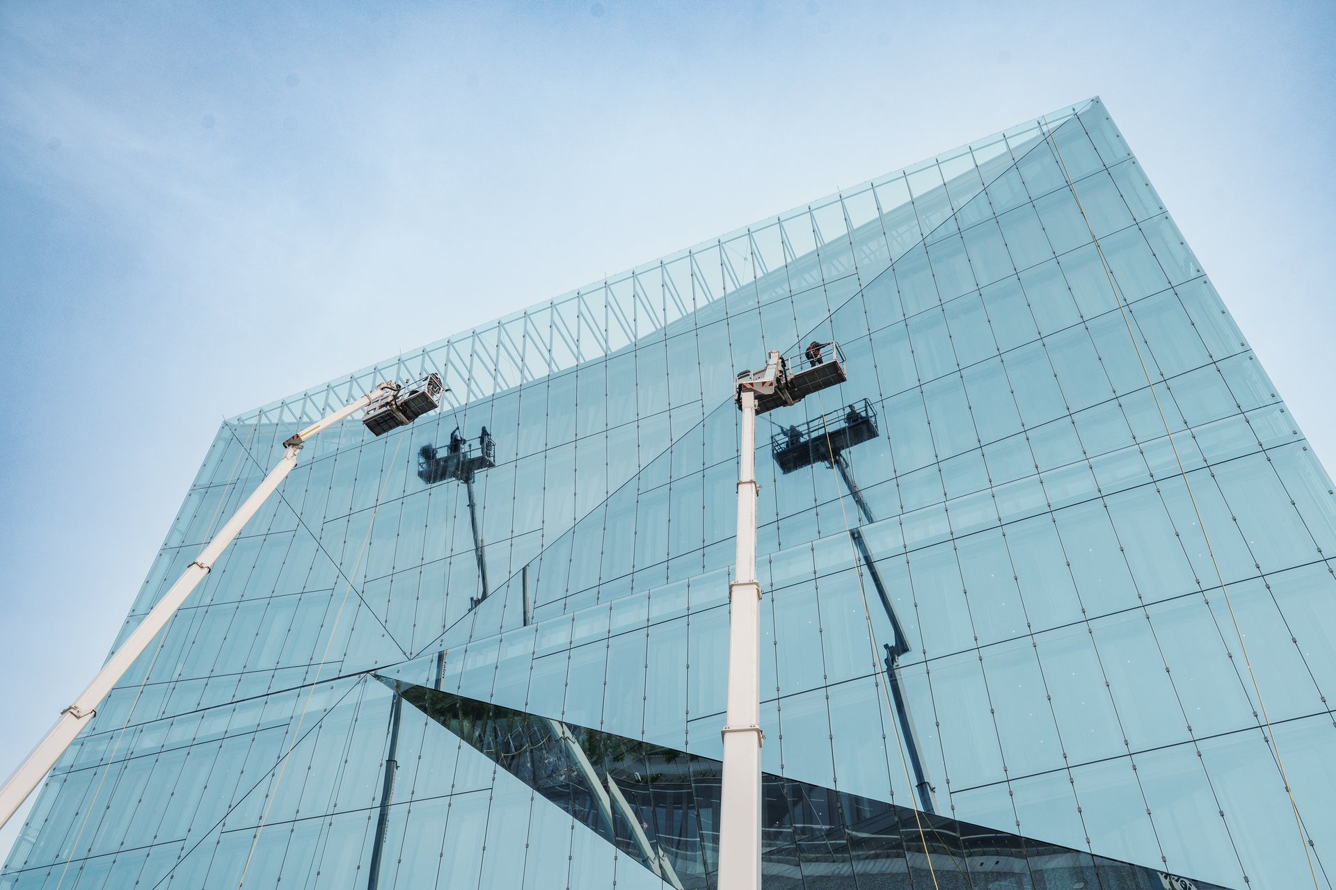 Workers using a mechanical lift to clean or maintain the reflective glass facade of a modern building