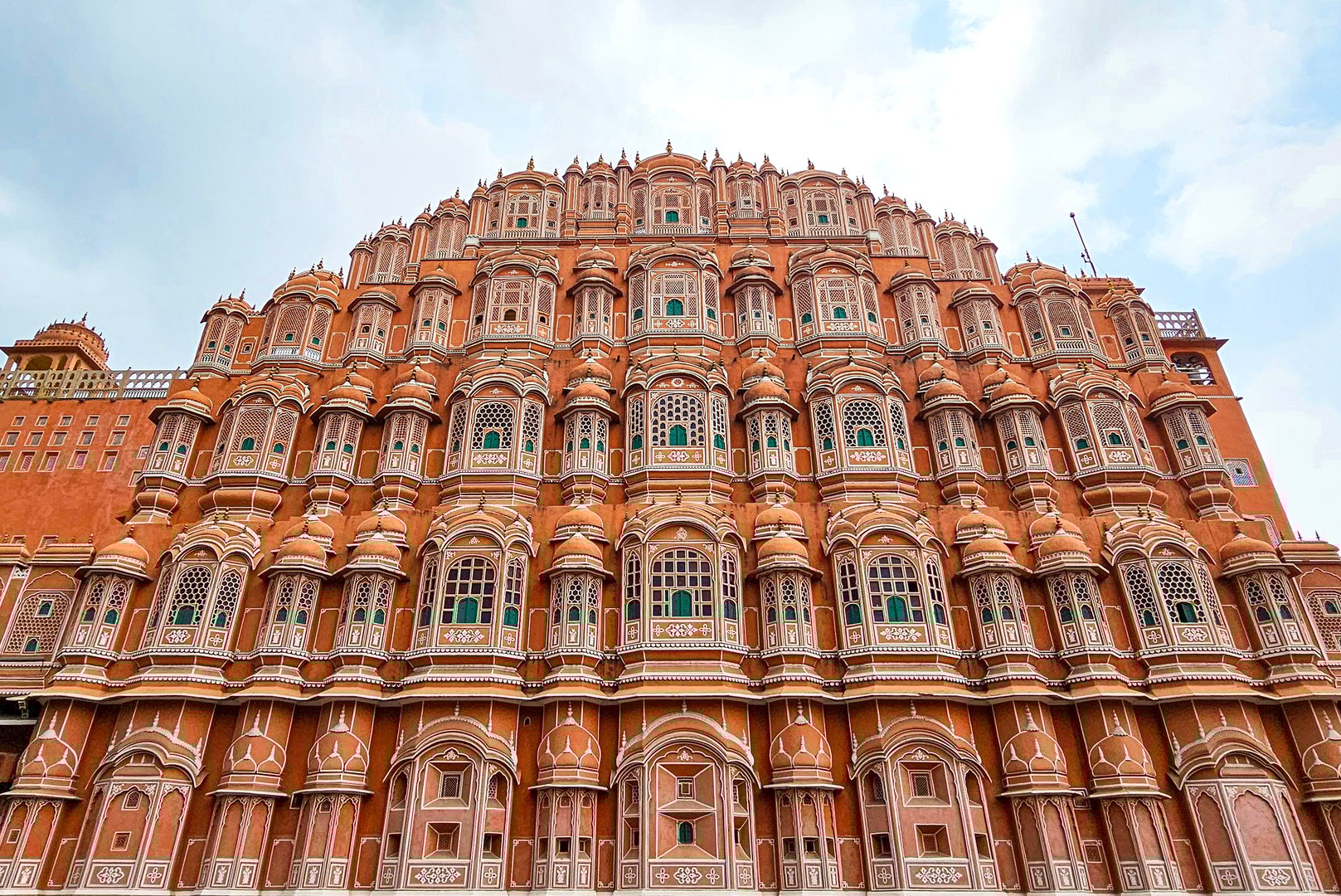 Jaipur, Rajasthan, India - 24 July, 2024: Hawa Mahal palace facade features intricate lattice windows and pink sandstone arches, showcasing a iconic Indian heritage landmark and Mughal-inspired design in a vibrant city setting.
