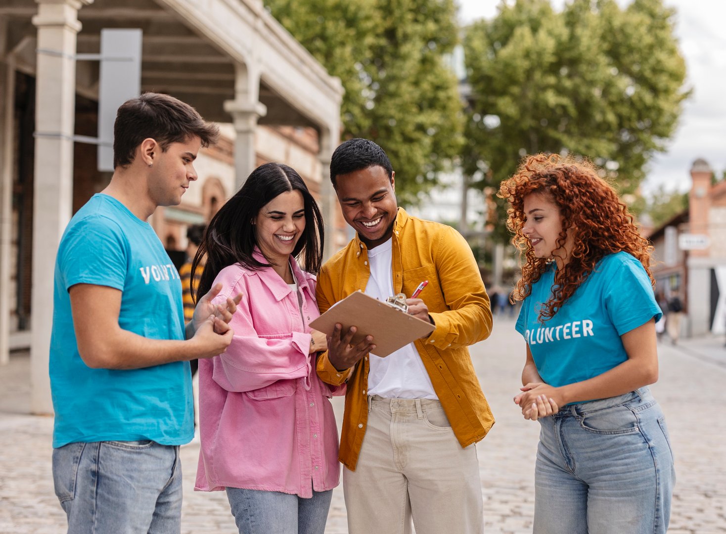 smiling couple signs a clipboard while talking to two volunteers at an outdoor community event.