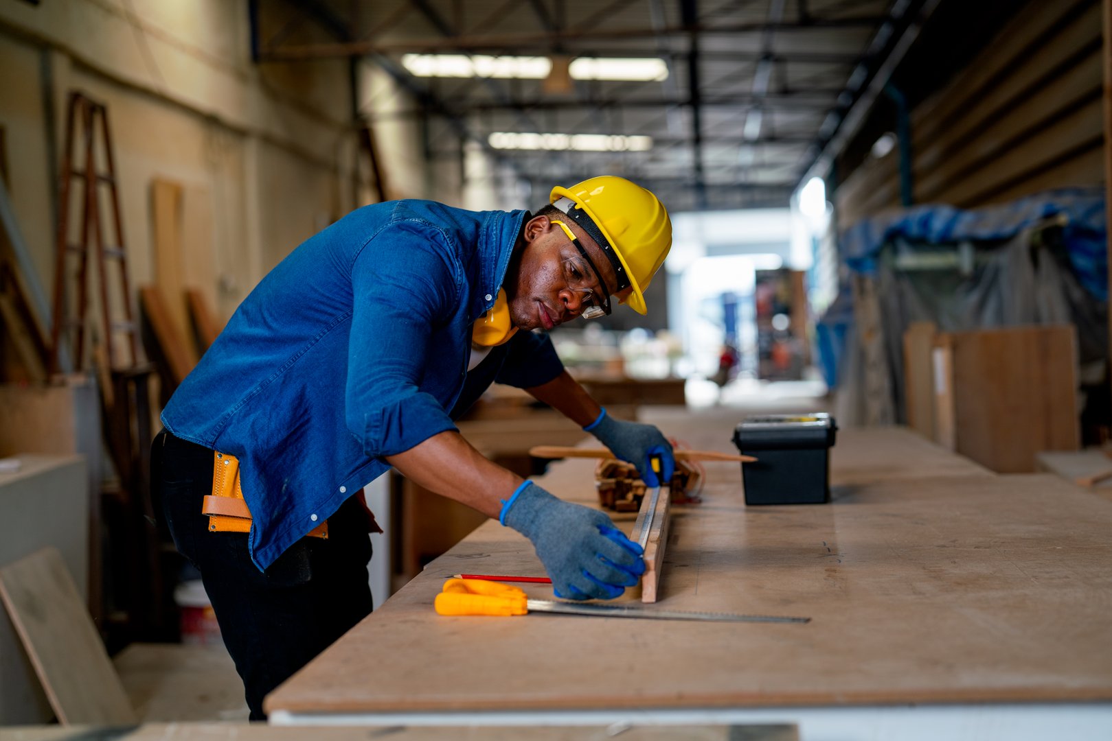 African American carpenter man use tape measure to work with timber on table during work in factory workplace area.