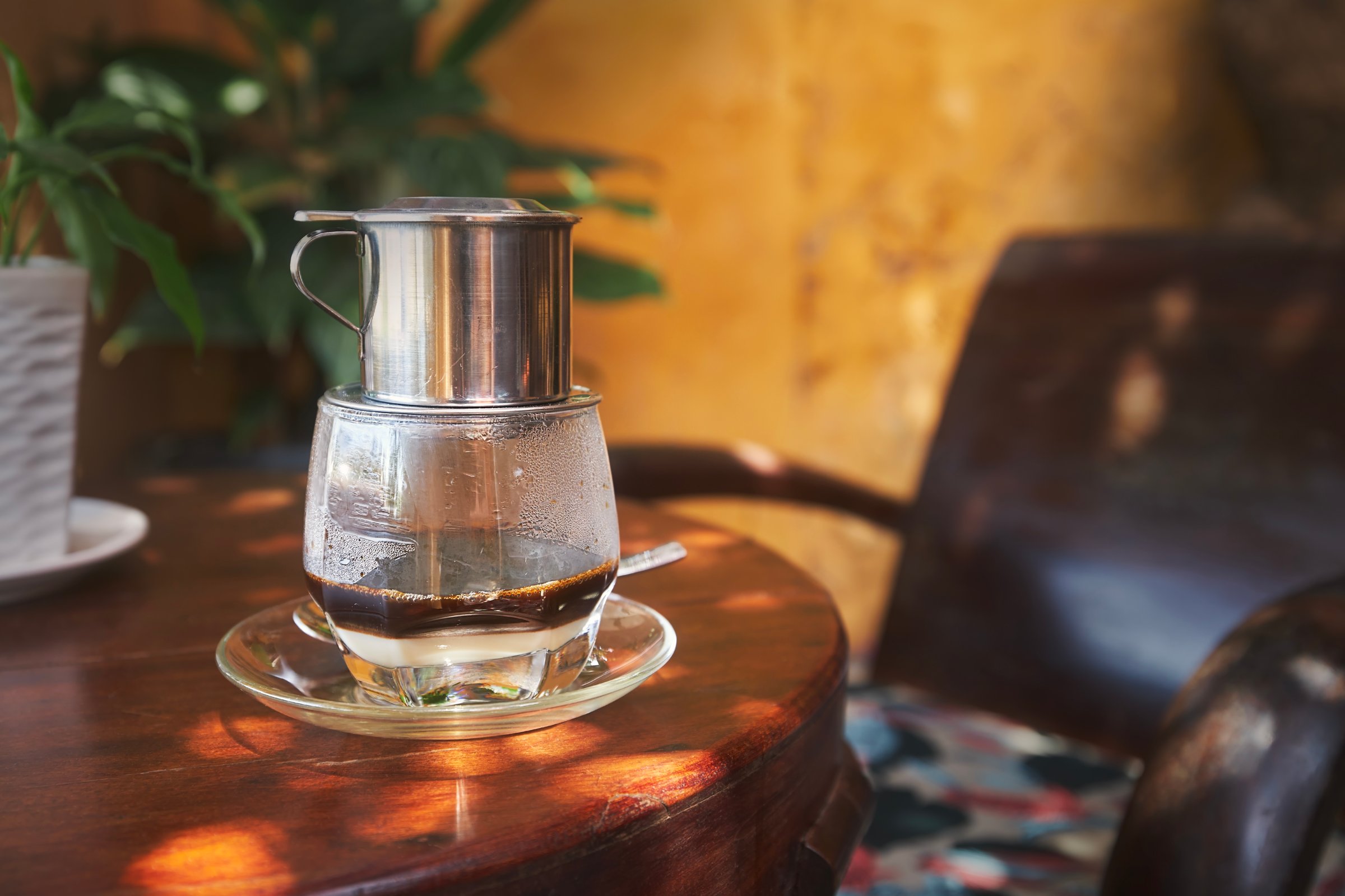 Glass of traditional hot Vietnamese coffee with condensed milk on wooden table in cafe in Vietnam.
