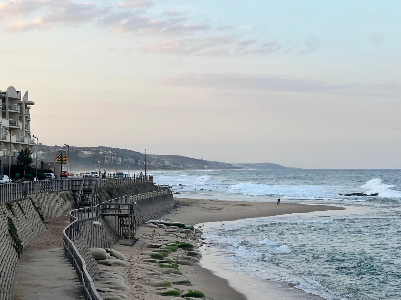 Beachfront apartment buildings overlooking a sandy beach and ocean waves with a pastel-colored sky at dusk.