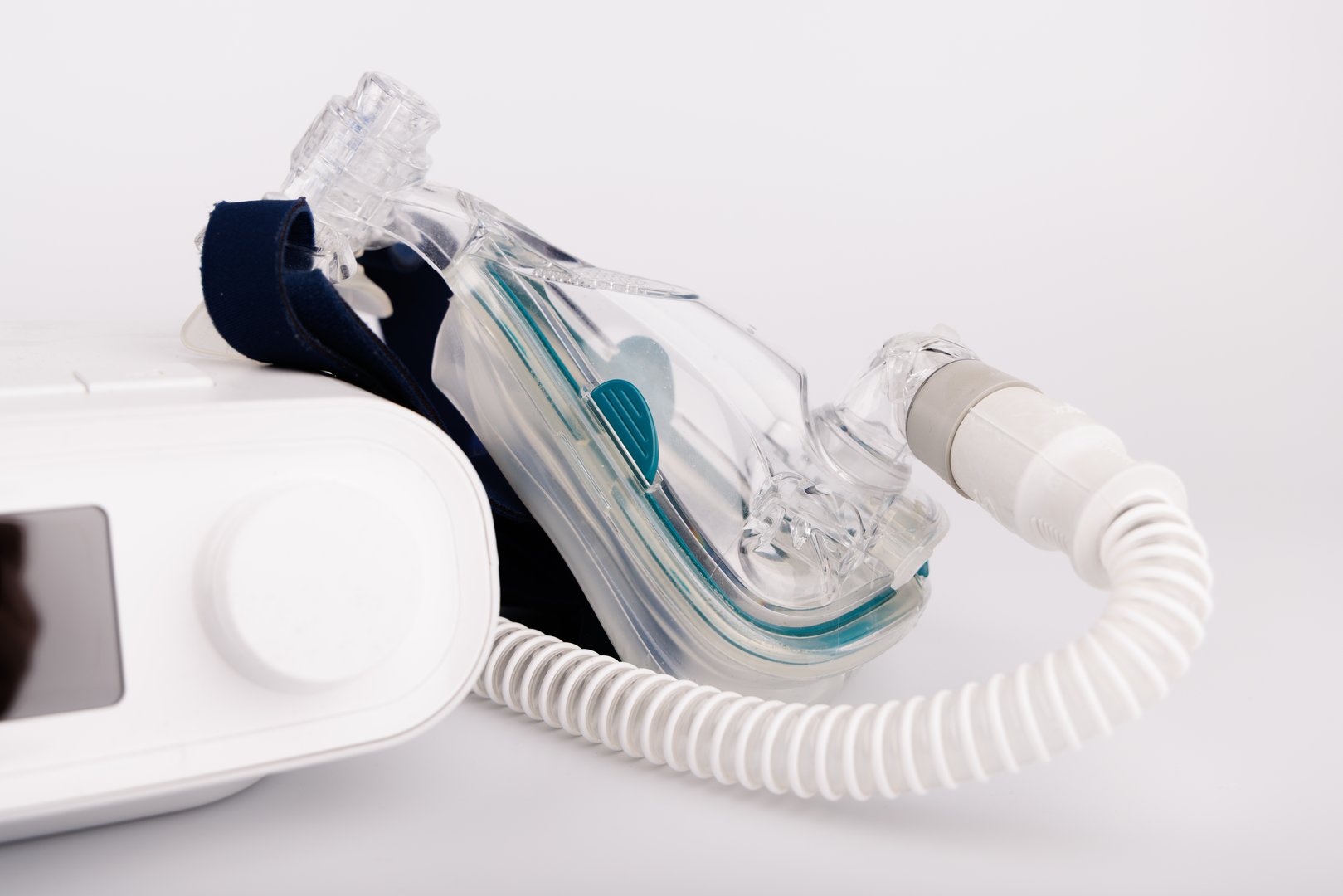 A white CPAP machine with a bright display, air hose, and breathing mask designed for sleep apnea treatment, isolated on a white background