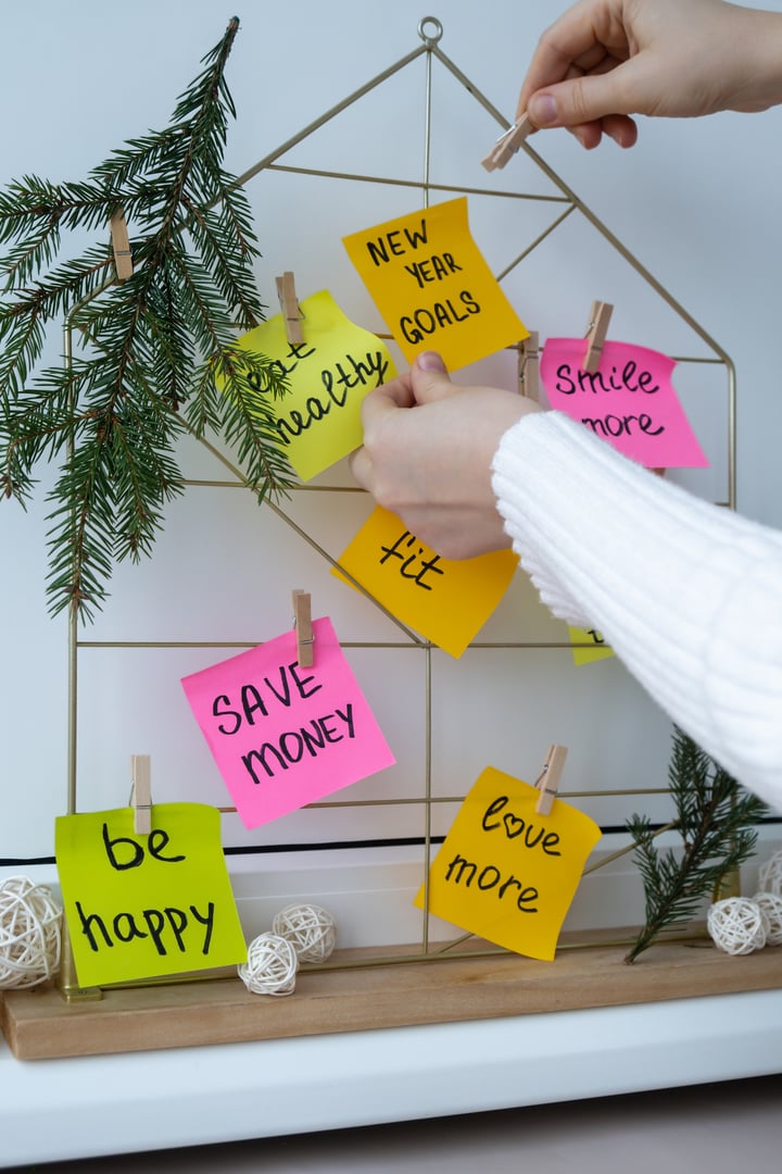 Female hands creating vision board with new year resolutions aims goals on sticky notes. Preparation for New Year. Concept of planning and setting goals for personal development