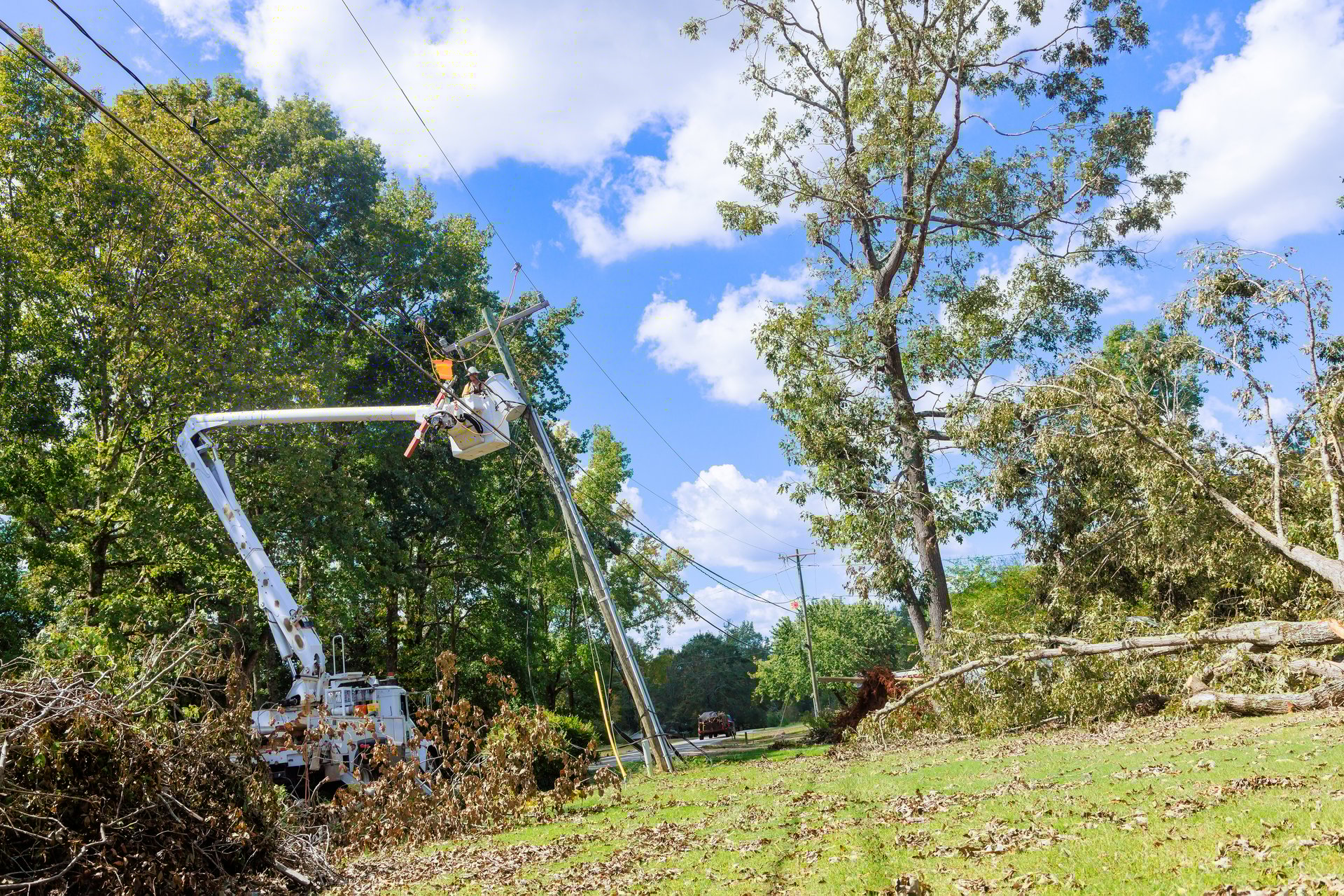 Utility workers in cherry picker clear branches restore service after storm damage