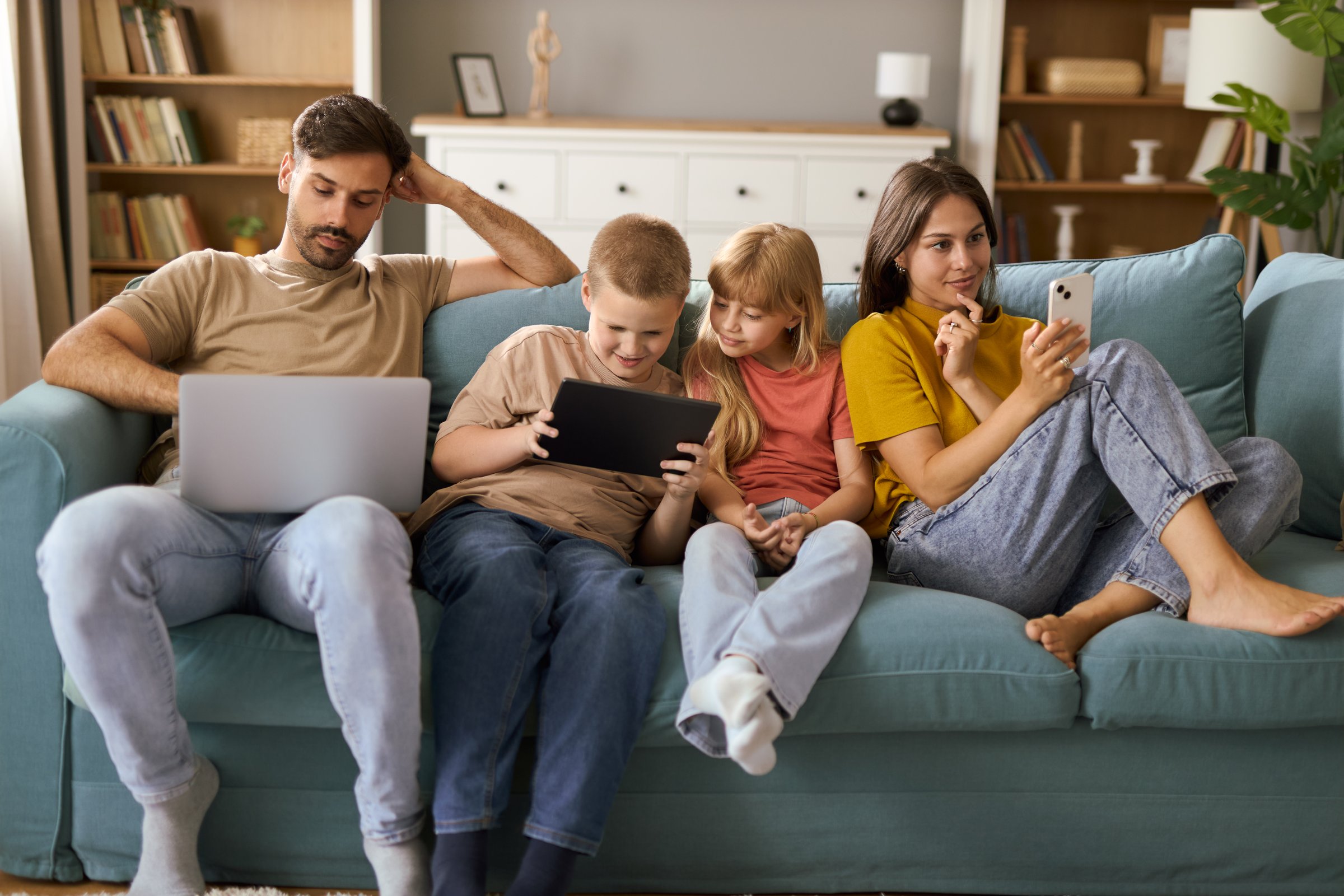 Young family using wireless technology while relaxing on sofa in the living room.