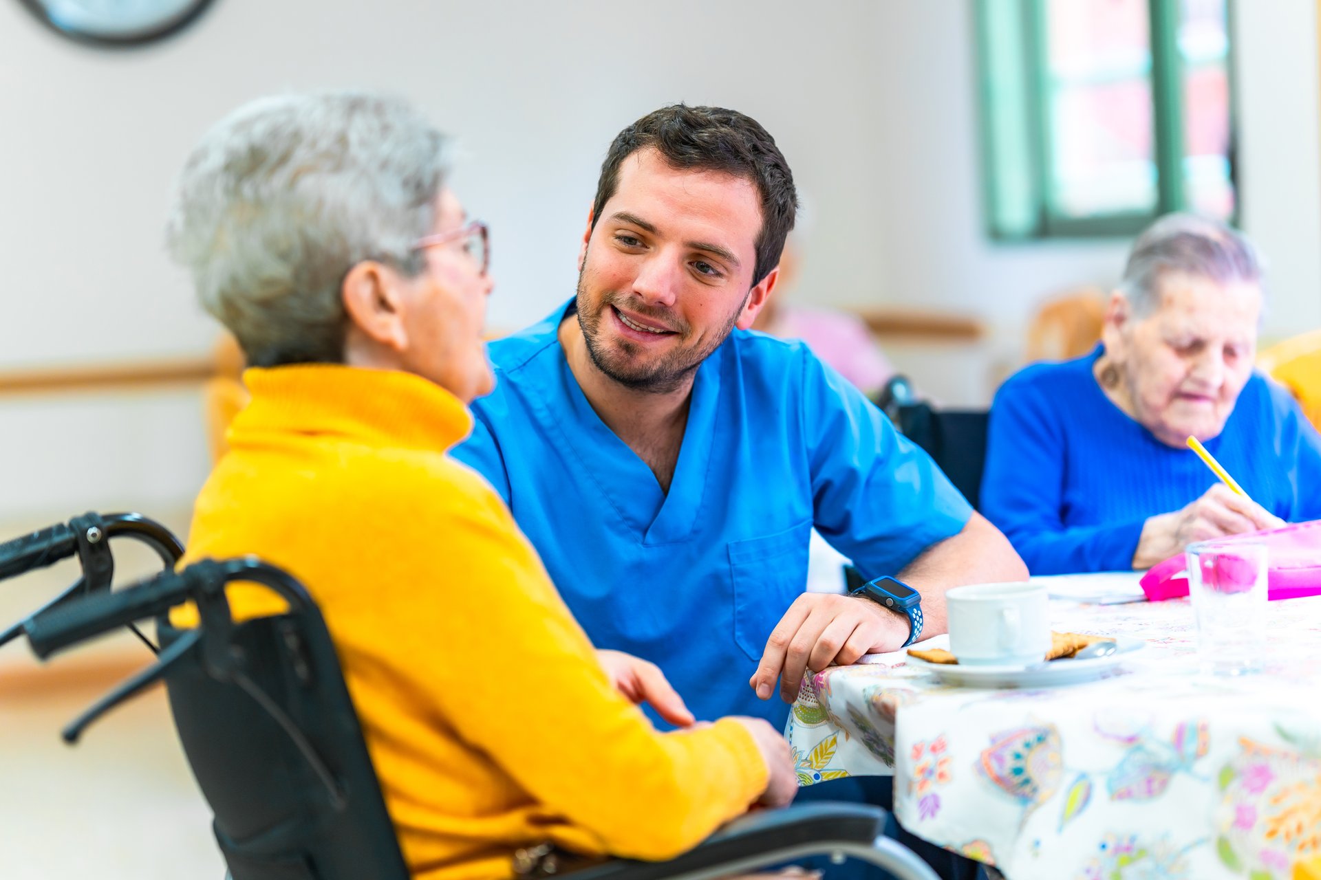 Male nurse is providing care and support to an elderly woman in a wheelchair at a nursing home, engaging in conversation and ensuring her well-being