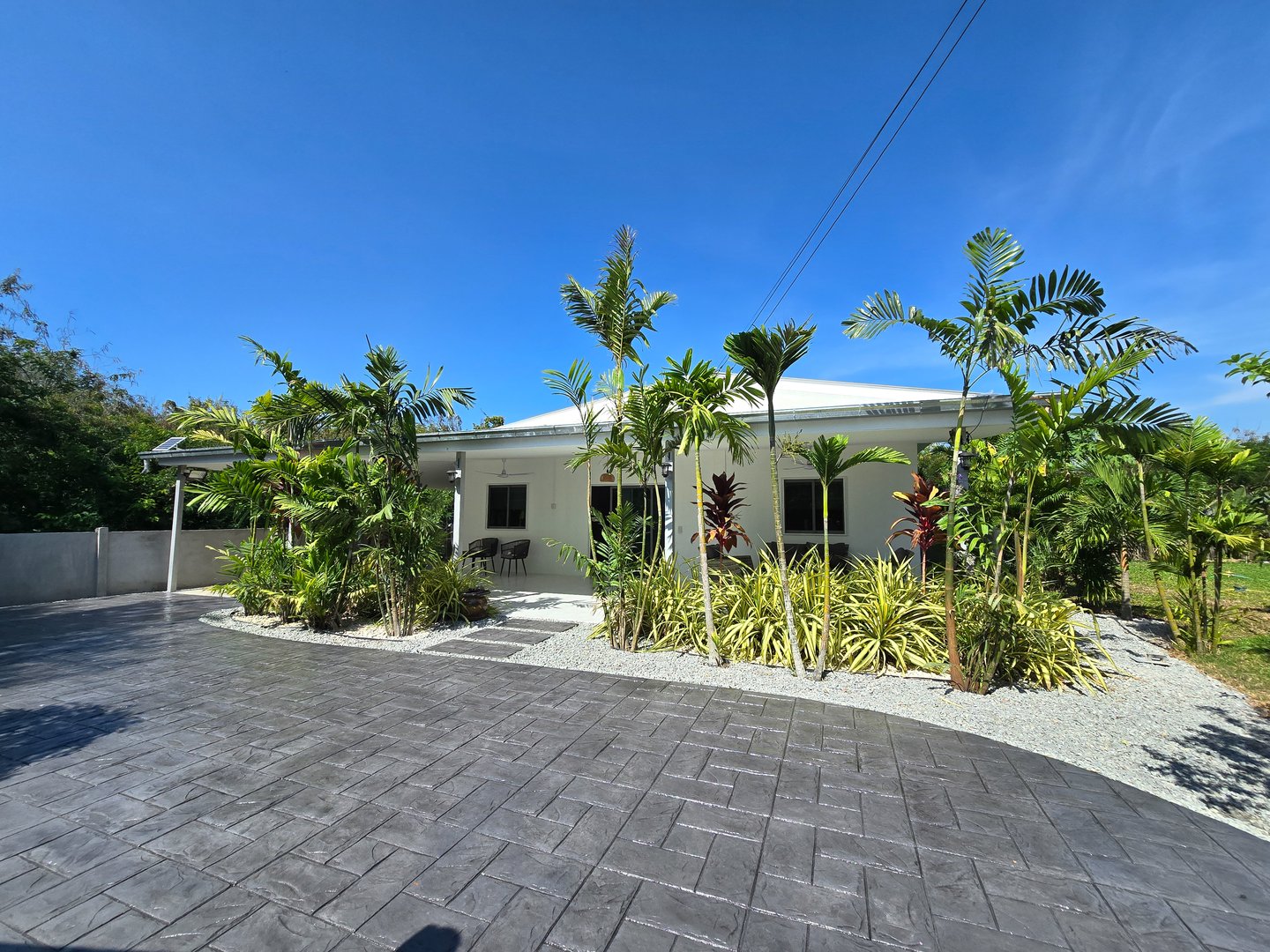 A vibrant modern home surrounded by lush greenery and tropical plants showcases a beautifully stamped concrete driveway. a Thai Suburban area with a modern family house