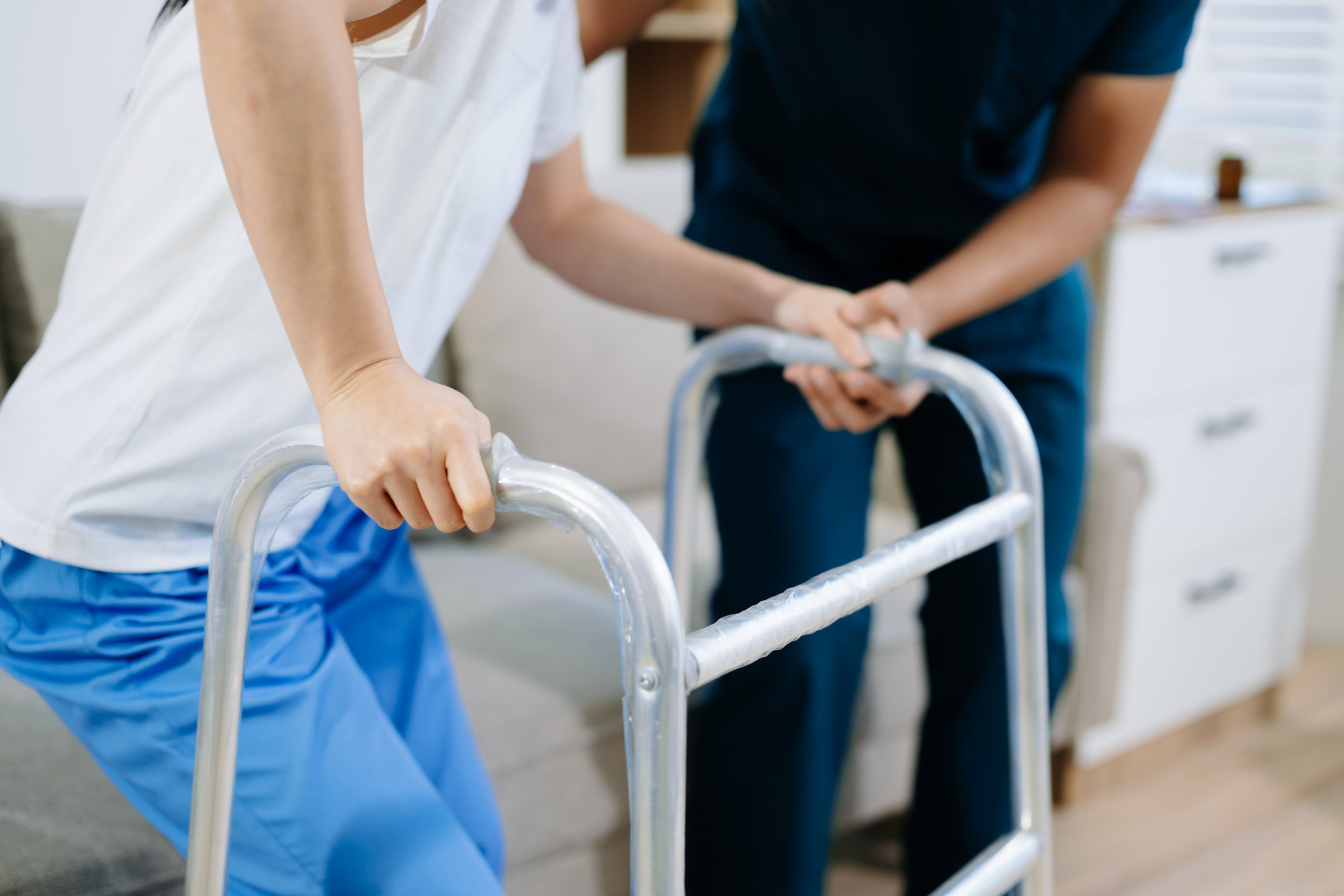 Close-up view of patient using walker during physical therapy with healthcare professional support, showing recovery, rehabilitation, and mobility training care.