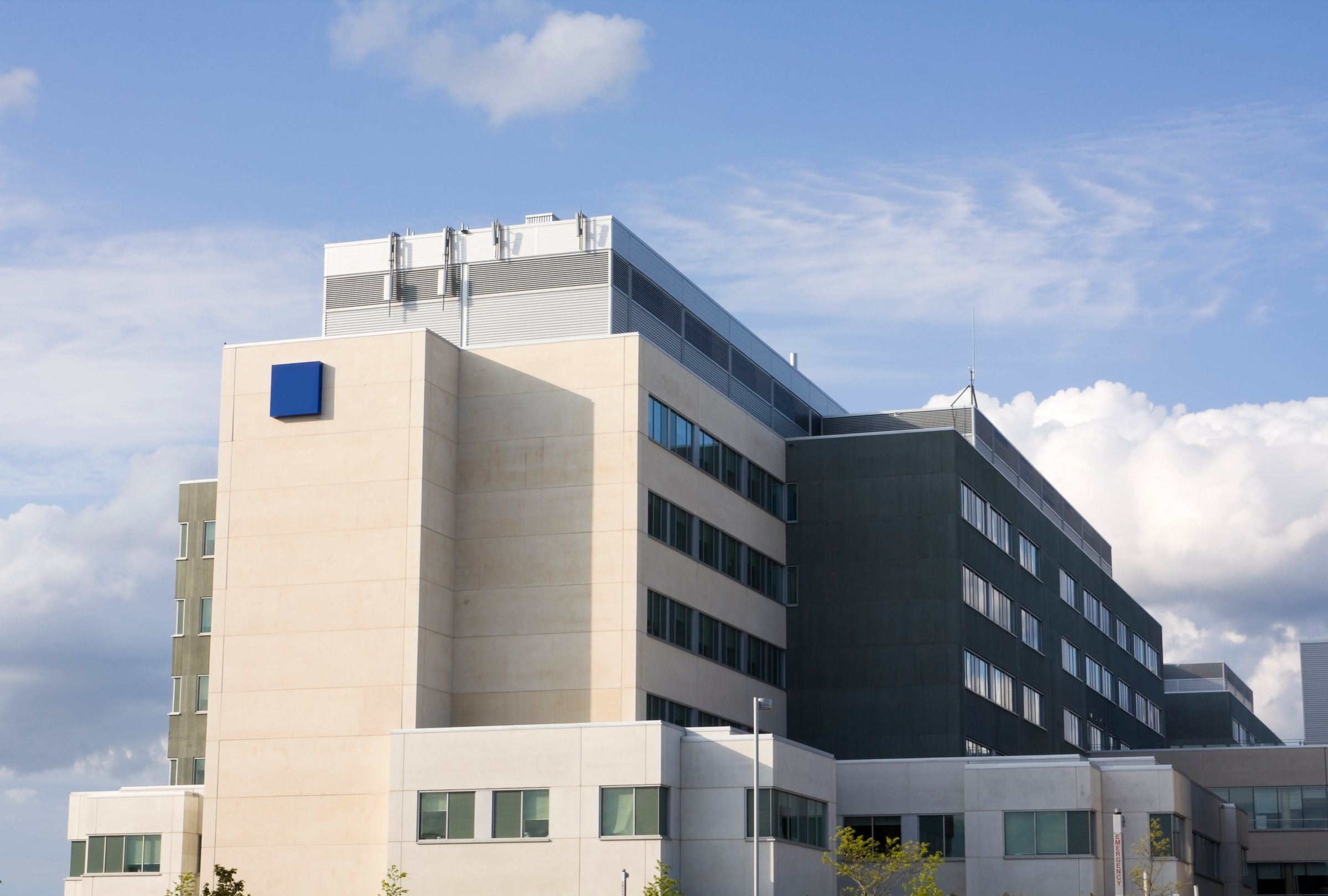 Modern multi-story building with beige and grey facade against a blue sky with clouds.