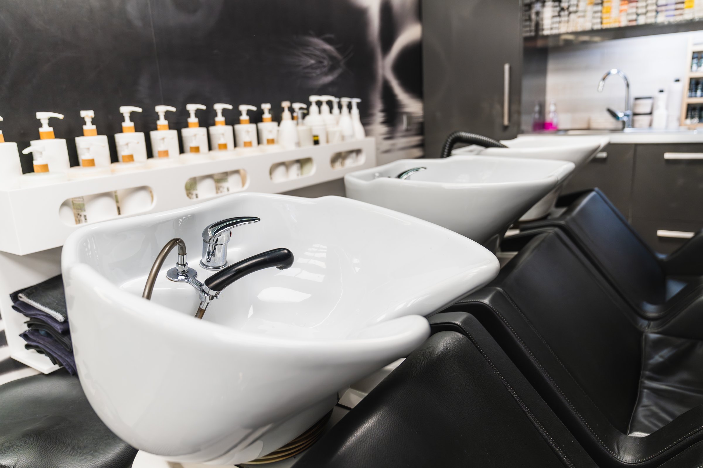 Hair salon interior featuring multiple shampoo sinks and comfortable chairs, ready for hair washing services