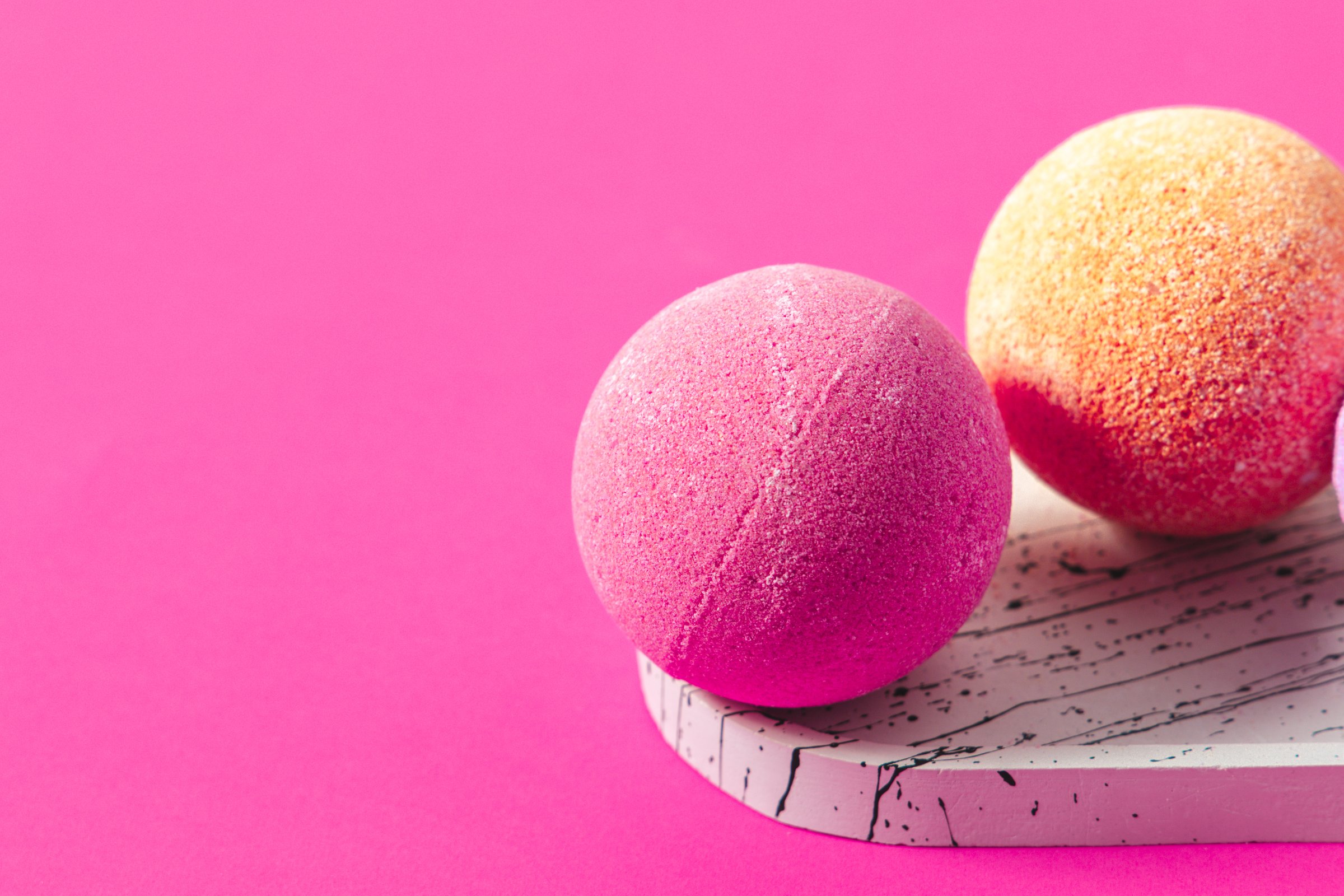 Bright pink and orange bath bombs are placed on a stylish marbled tray highlighting their textures and colors.