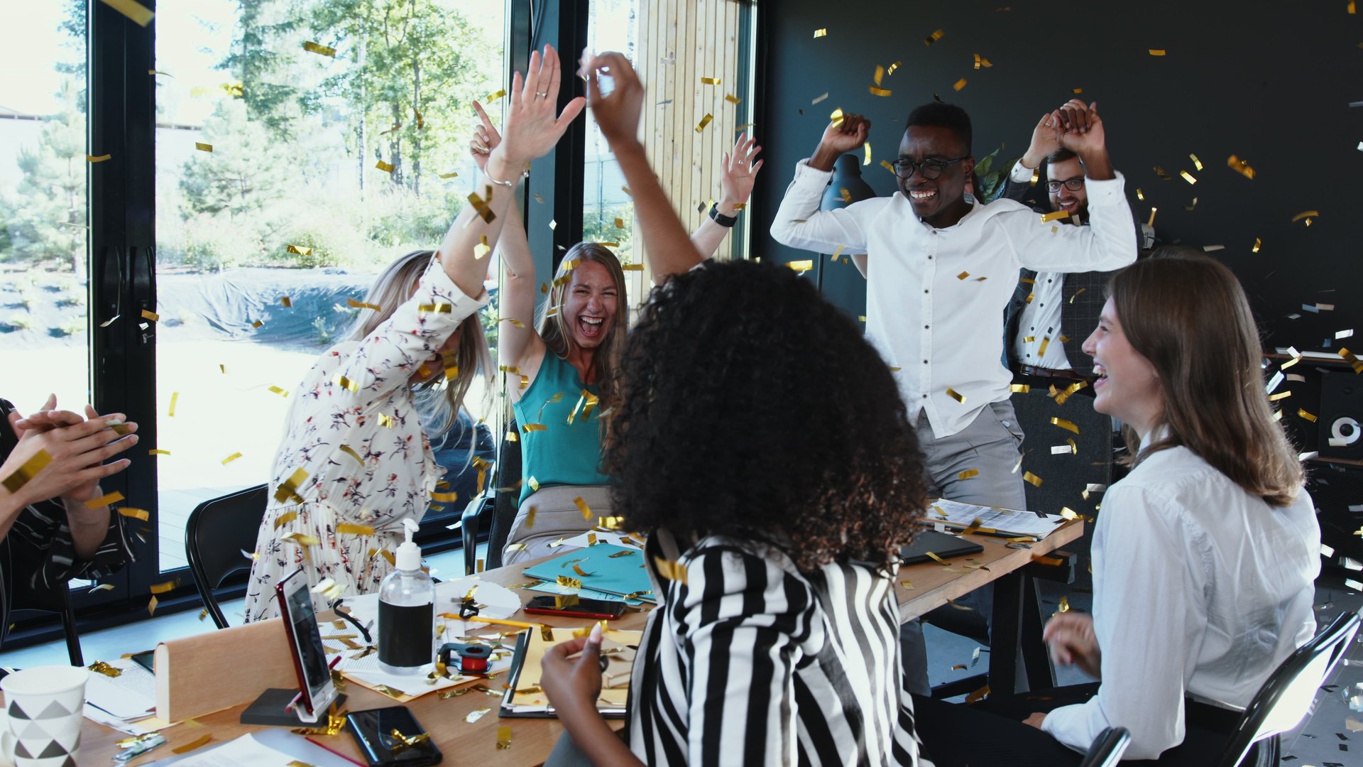 Coronavirus lockdown ending. Happy multiethnic business team taking masks off, celebrate victory with confetti at office. Start-up partners are excited with normal life after quarantine break.