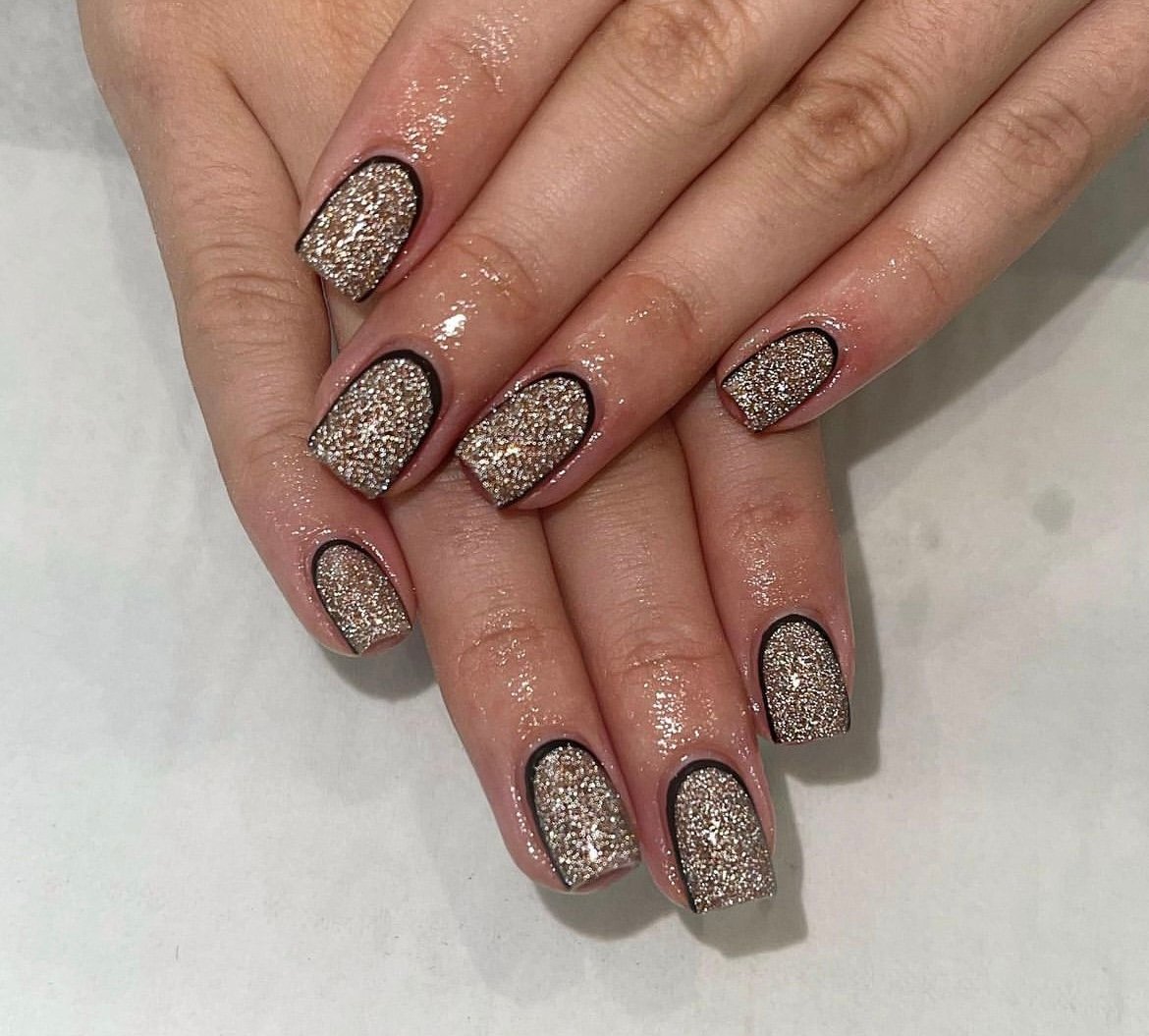 Hands with glittery gold nails featuring black outlines on a light background.