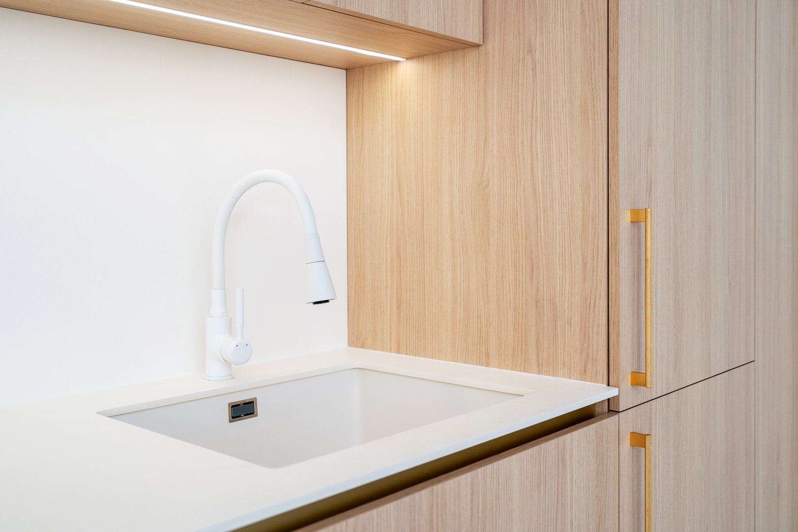 Close up shot of contemporary kitchen features a sleek white sink and faucet set against copy space backgrounds. The clean lines and modern finishes create a stylish and functional space in room