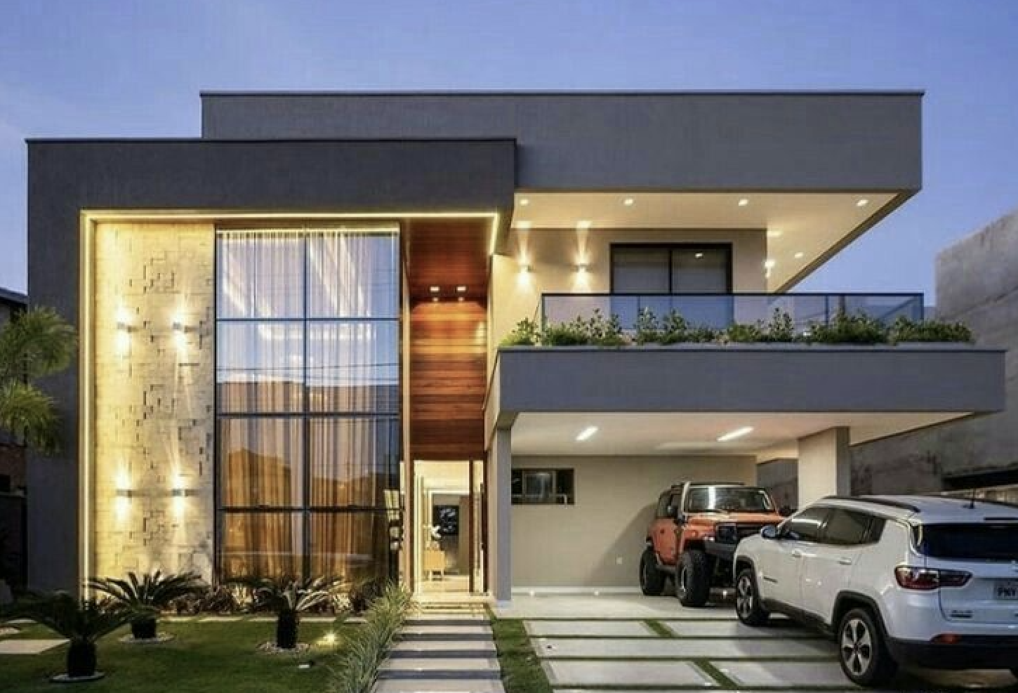 Modern two-story house with large windows, a balcony, and a garage with two parked cars at dusk.
