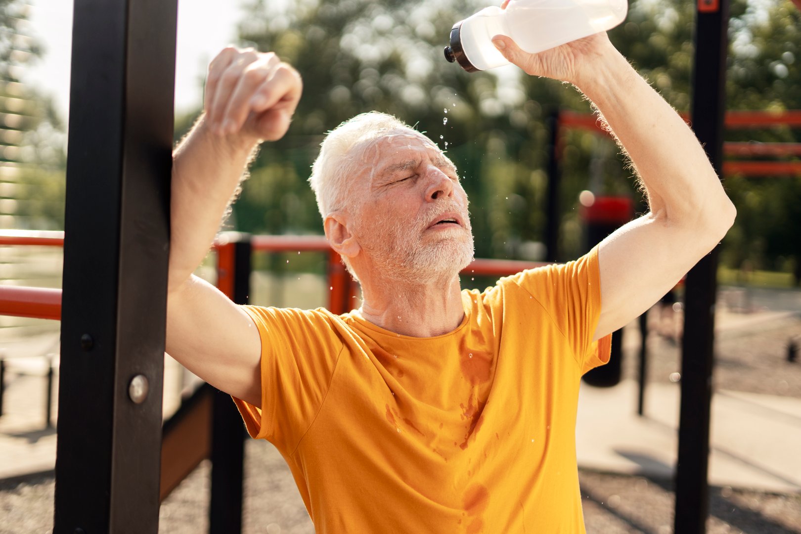 Exhausted sportsman pouring water on his face after exercising on a hot summer day