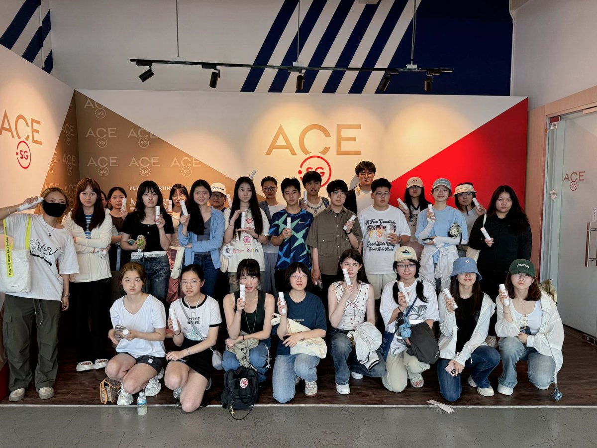 Group of people posing in front of a wall with ACE logo, holding ice creams, some wearing hats and masks.