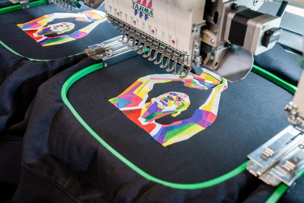 Embroidery machine stitching colorful geometric design on black fabric.