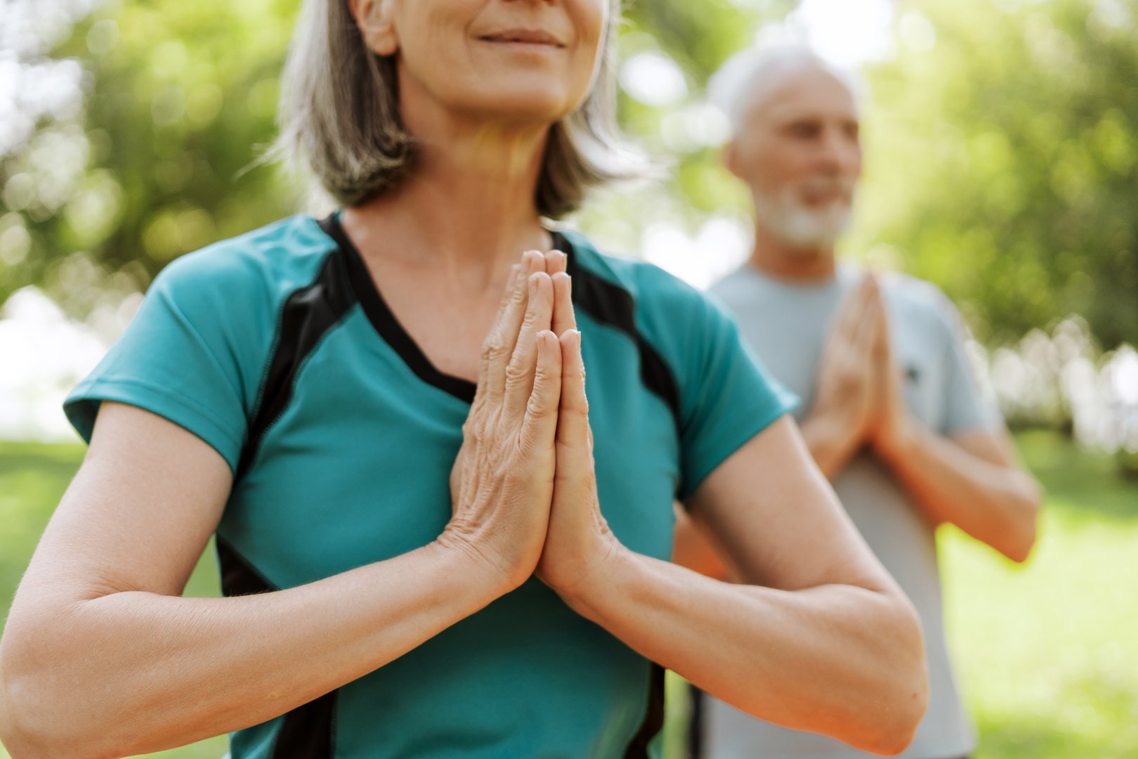 Senior couple practicing yoga together outdoors in the park selective focus on hands outdoors. Active lifestyle concept