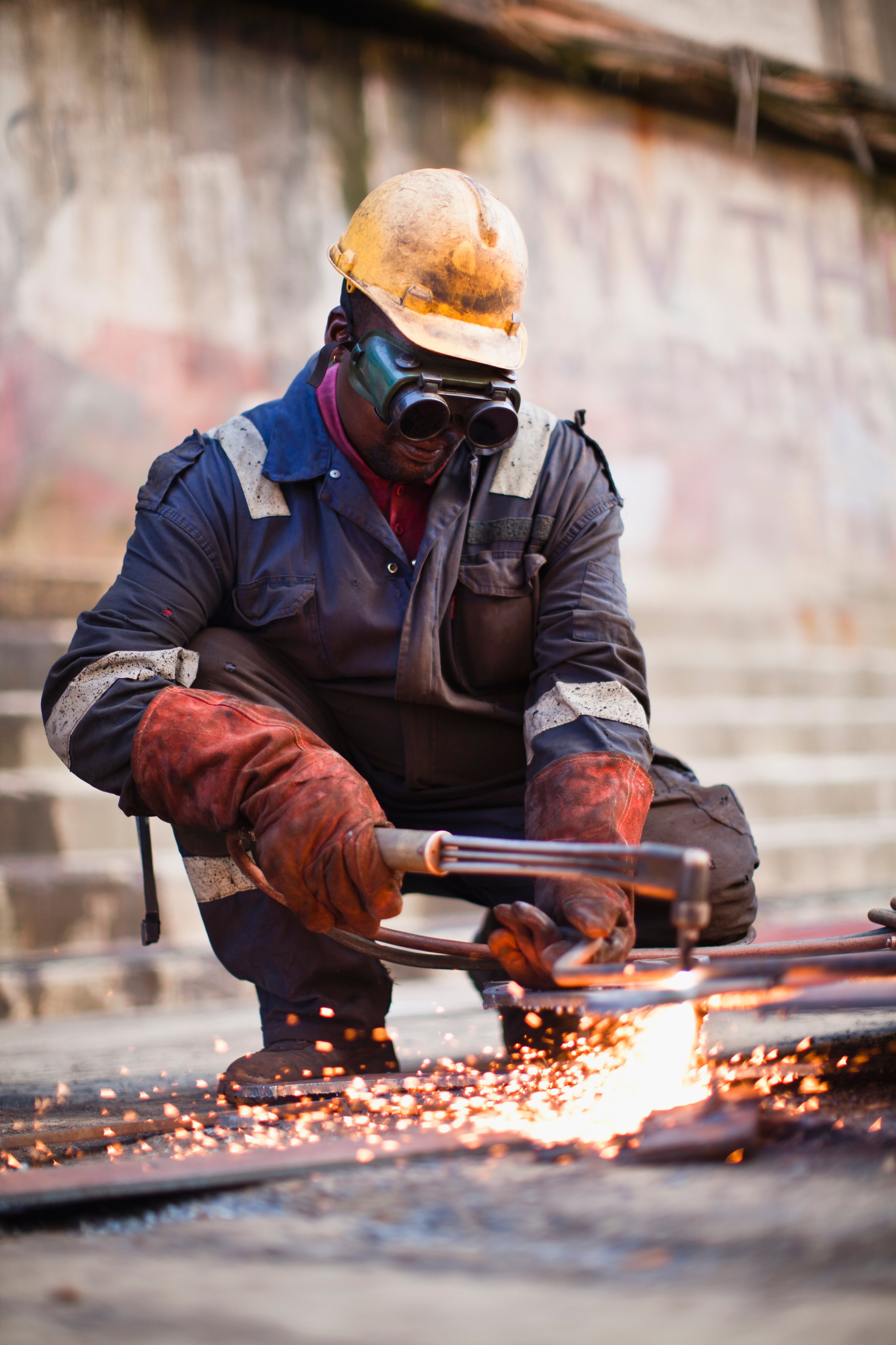 Metalworker wearing protective gear, using a blowtorch to cut metal, with bright sparks flying around.