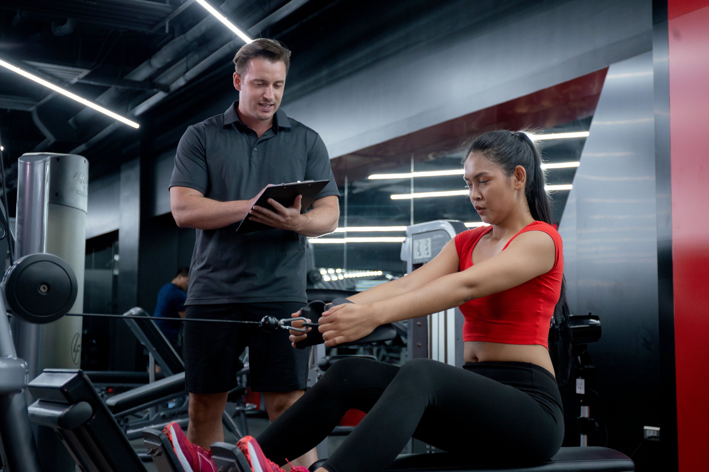 Coach man guiding workout with hands muscles stretch with equipment machine with woman in fitness gym club, strength and flexibility training, woman exercise with instructor or trainer, sport concept.
