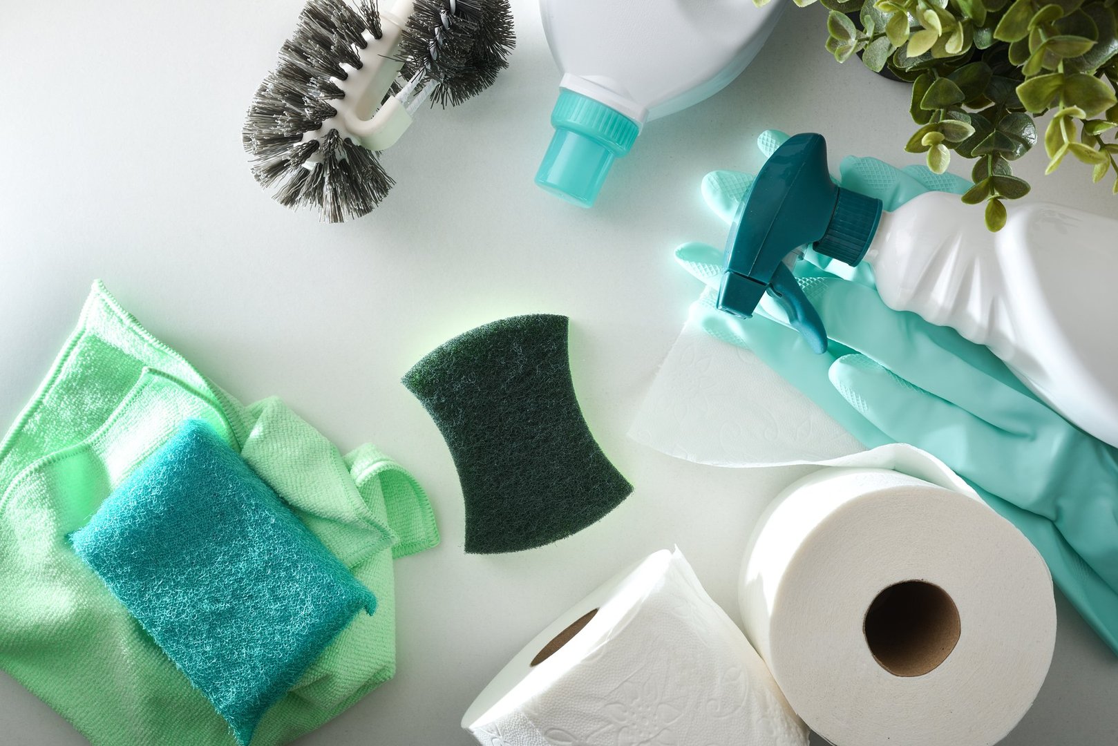 Bathroom cleaning supplies such as disinfectant bottles, scouring pads, gloves, toilet brush and toilet paper on white wooden table. Top view.