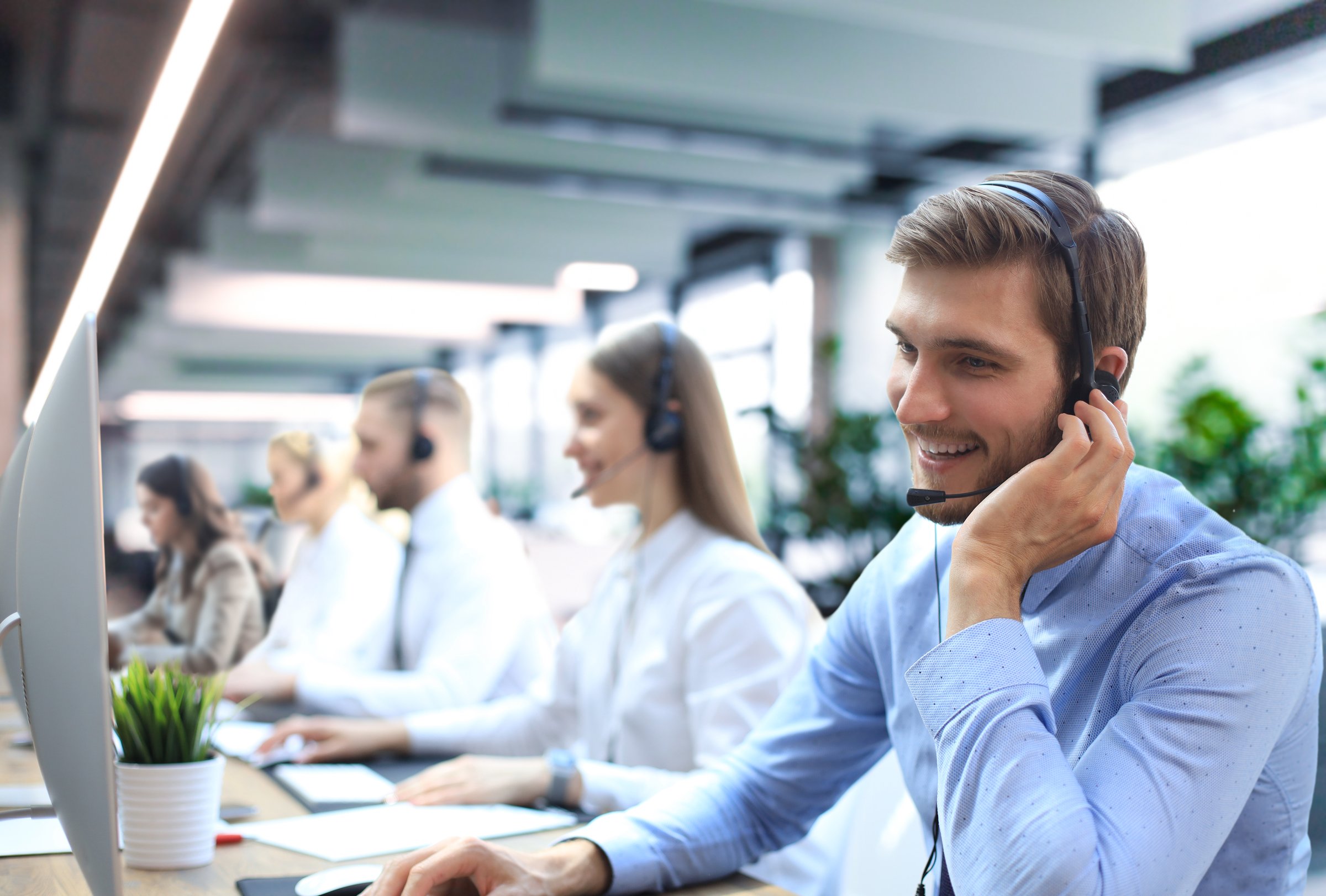 Portrait of call center worker accompanied by his team. Smiling customer support operator at work
