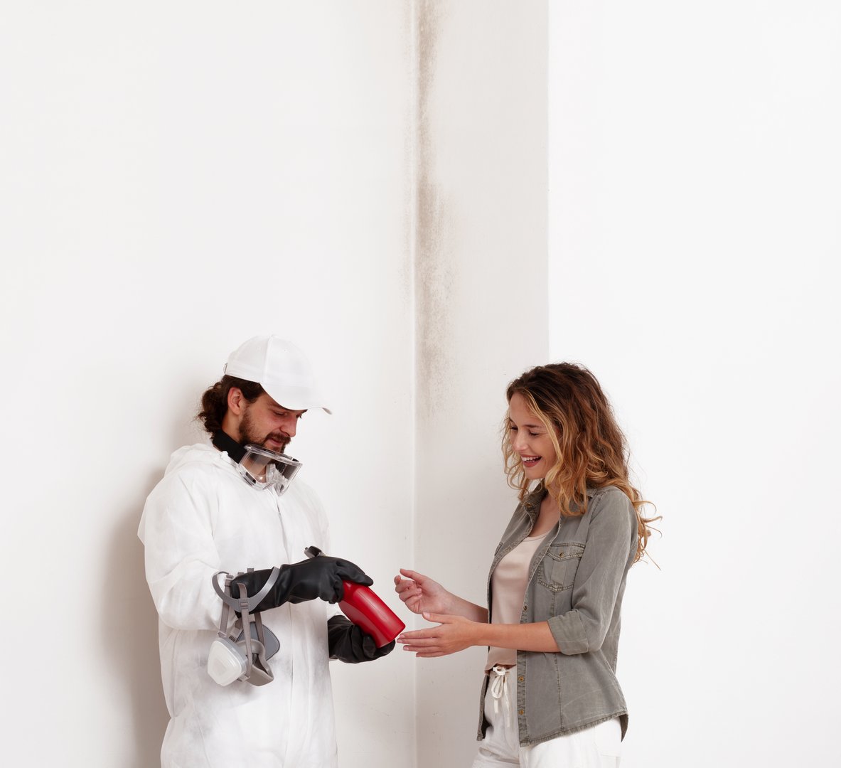 A professional worker shows mold remediation products to a smiling woman customer at a home renovation site with mold problems on the walls. Wall painting, cleaning, and mold removal services concept
