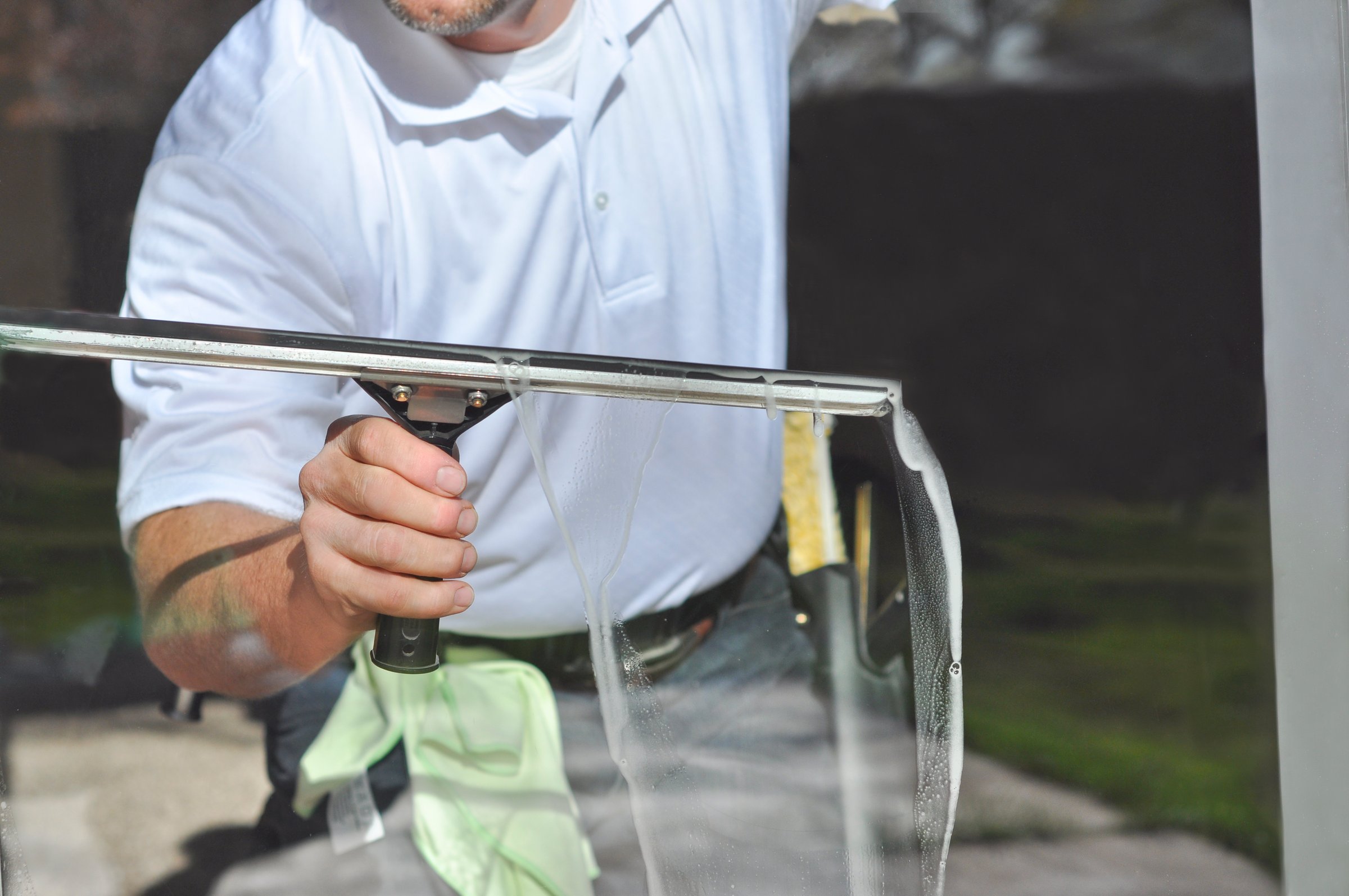 A window cleaning professional uses a large squeegee to clean the water and soap suds off of a residential window.