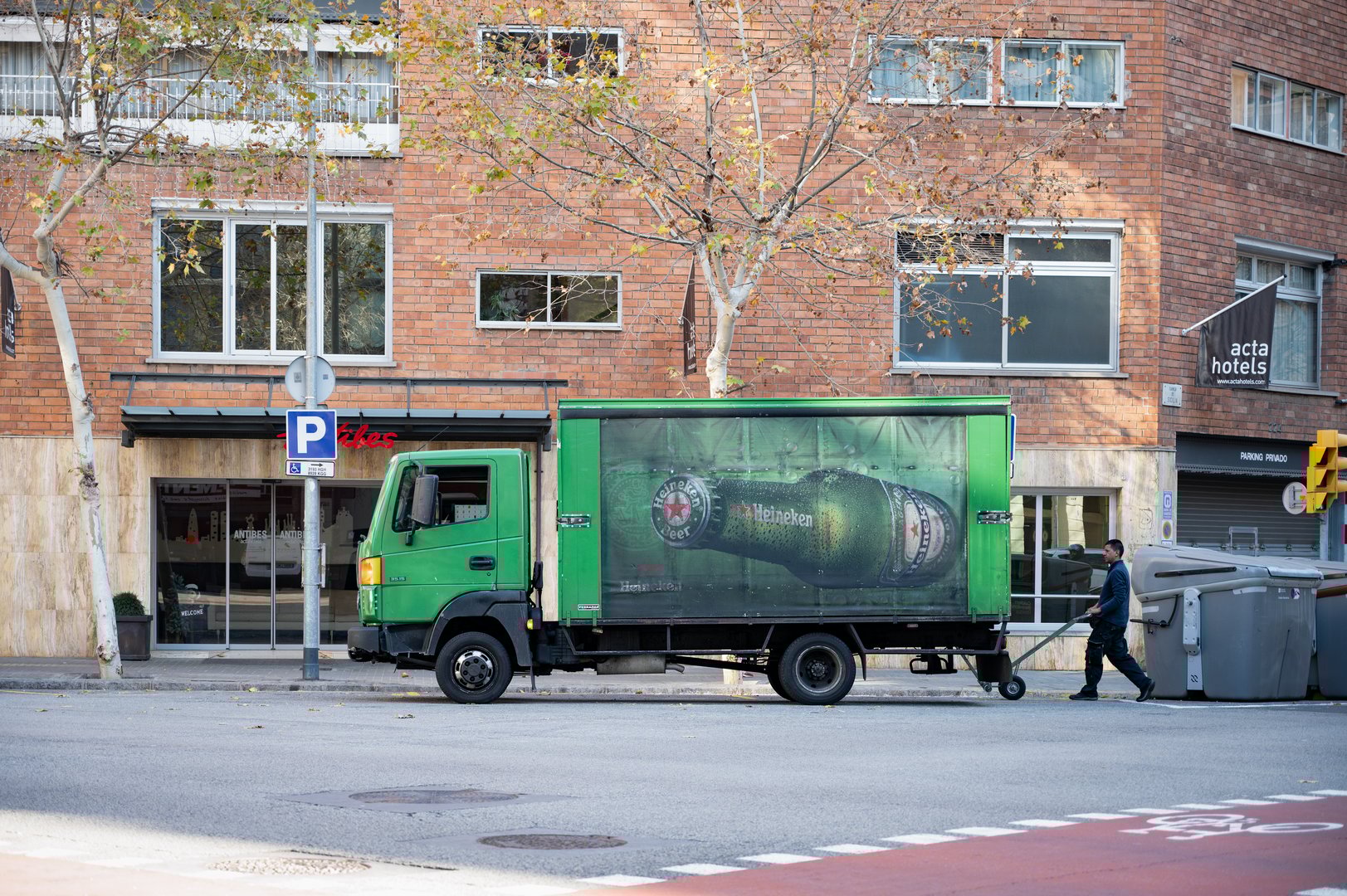 Side view of a green Heineken beer delivery truck stopped on a corner in double row in the city of Barcelona