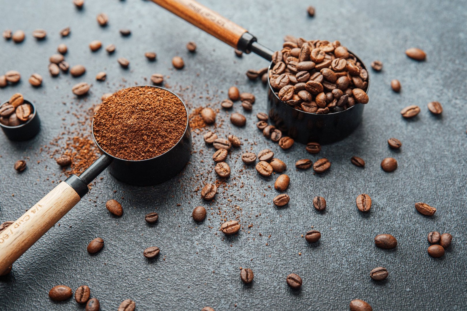 Ground coffee and whole beans with scoops on gray background