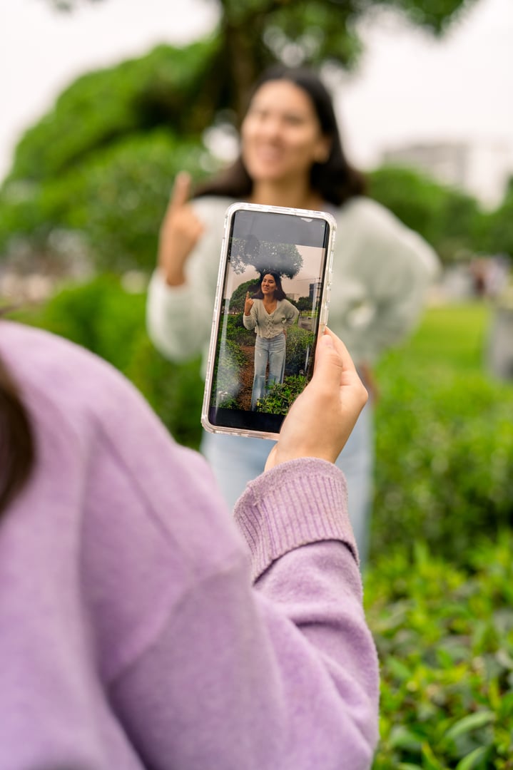 Young adult woman filming her friend with a smartphone, creating content outdoors for social media