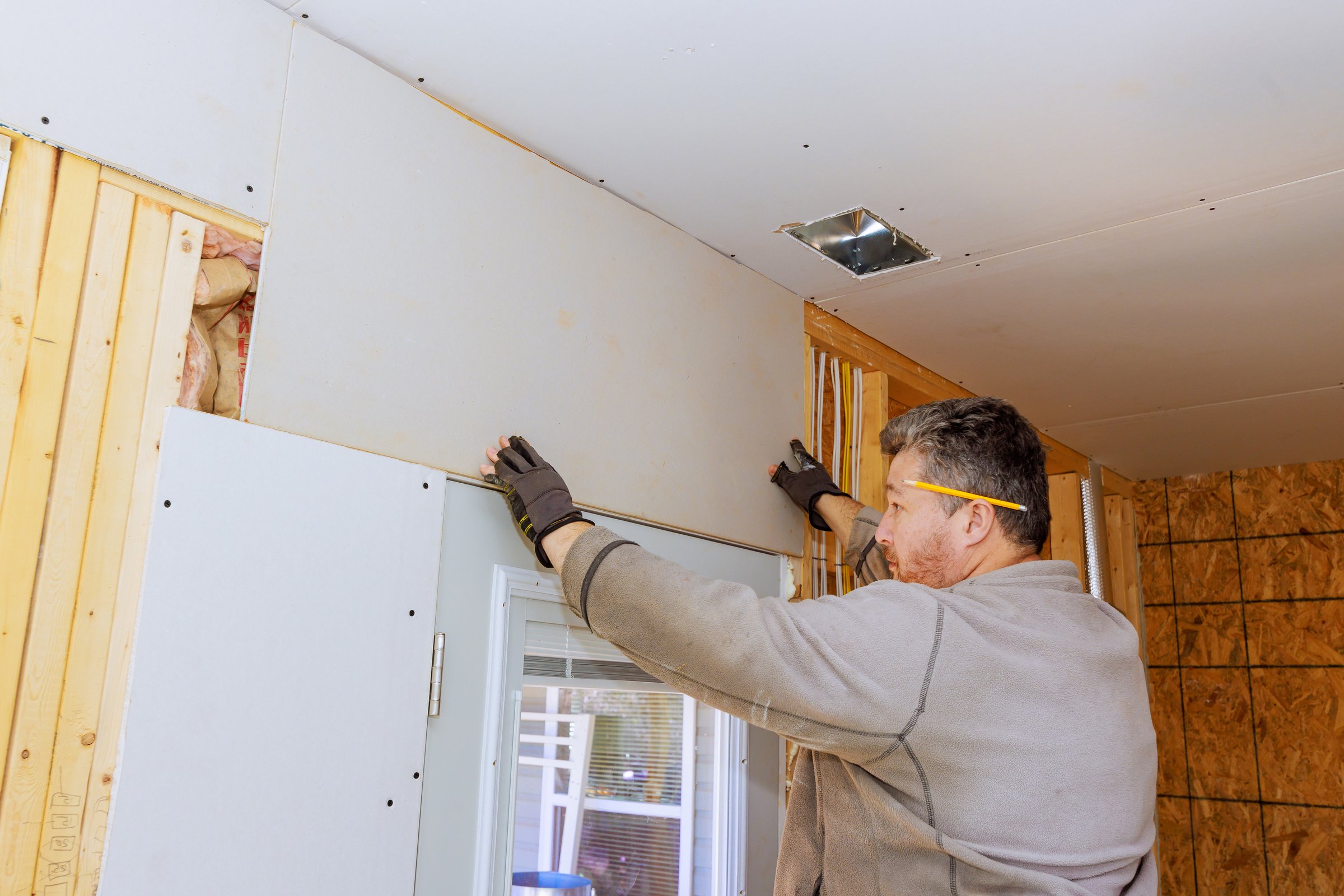 Carpenter is carefully placing drywall sheetrock sheets on interior wall during home renovation