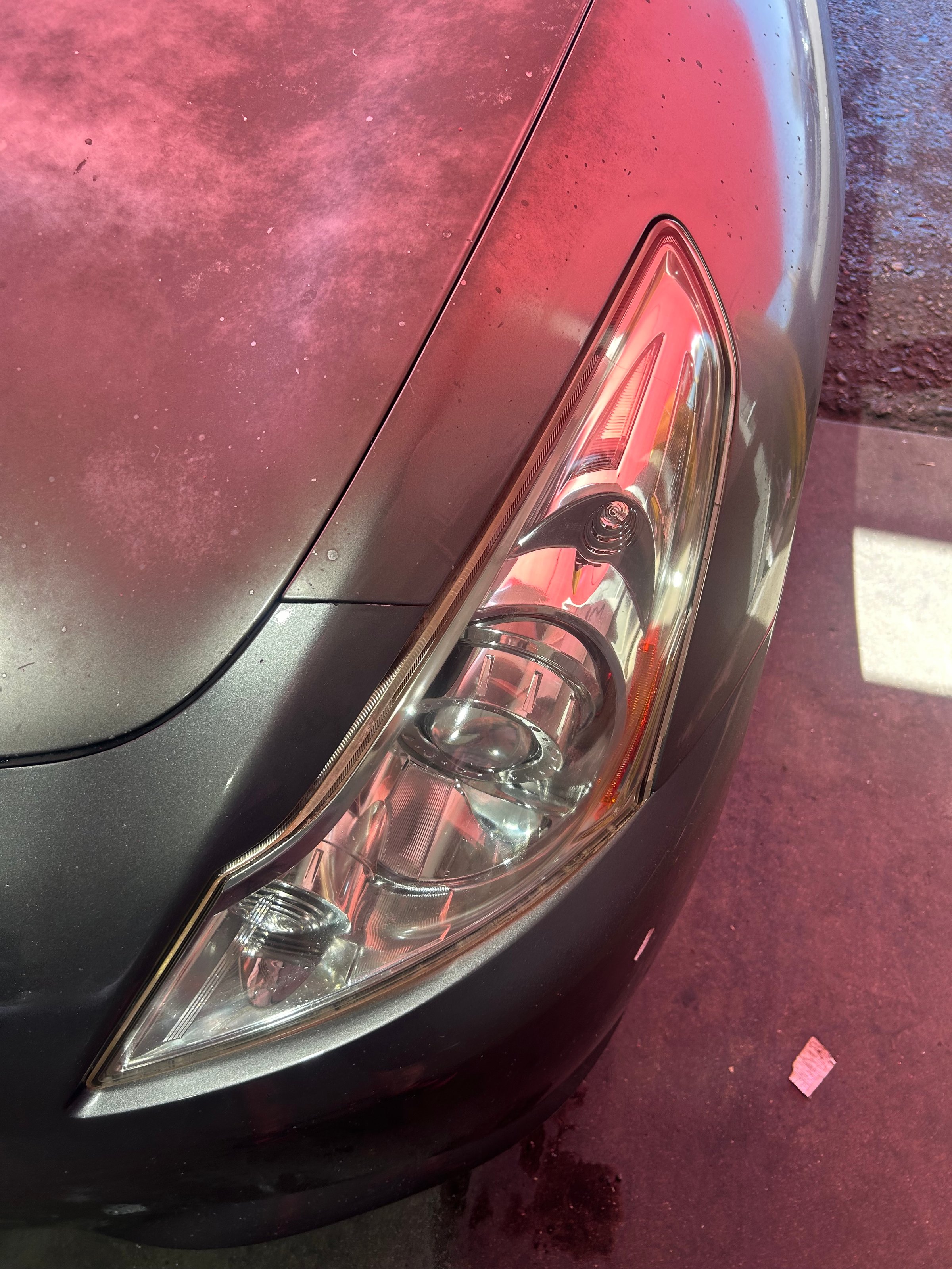 Close-up of a car's front headlight with a glossy black and red tint under bright lighting.