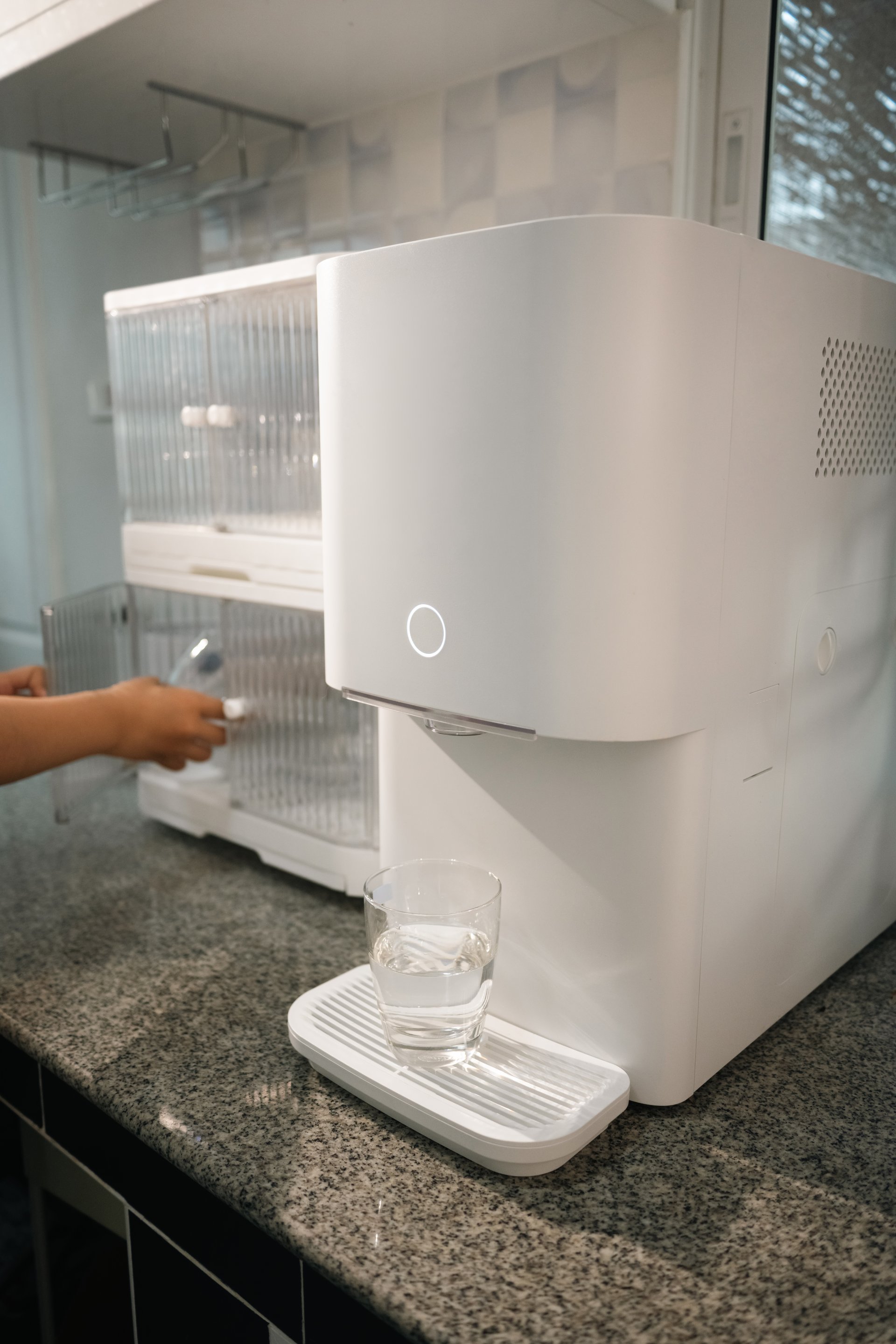 Modern water purifier dispensing clean water into a glass on kitchen countertop. Healthy living and smart home appliances concept.