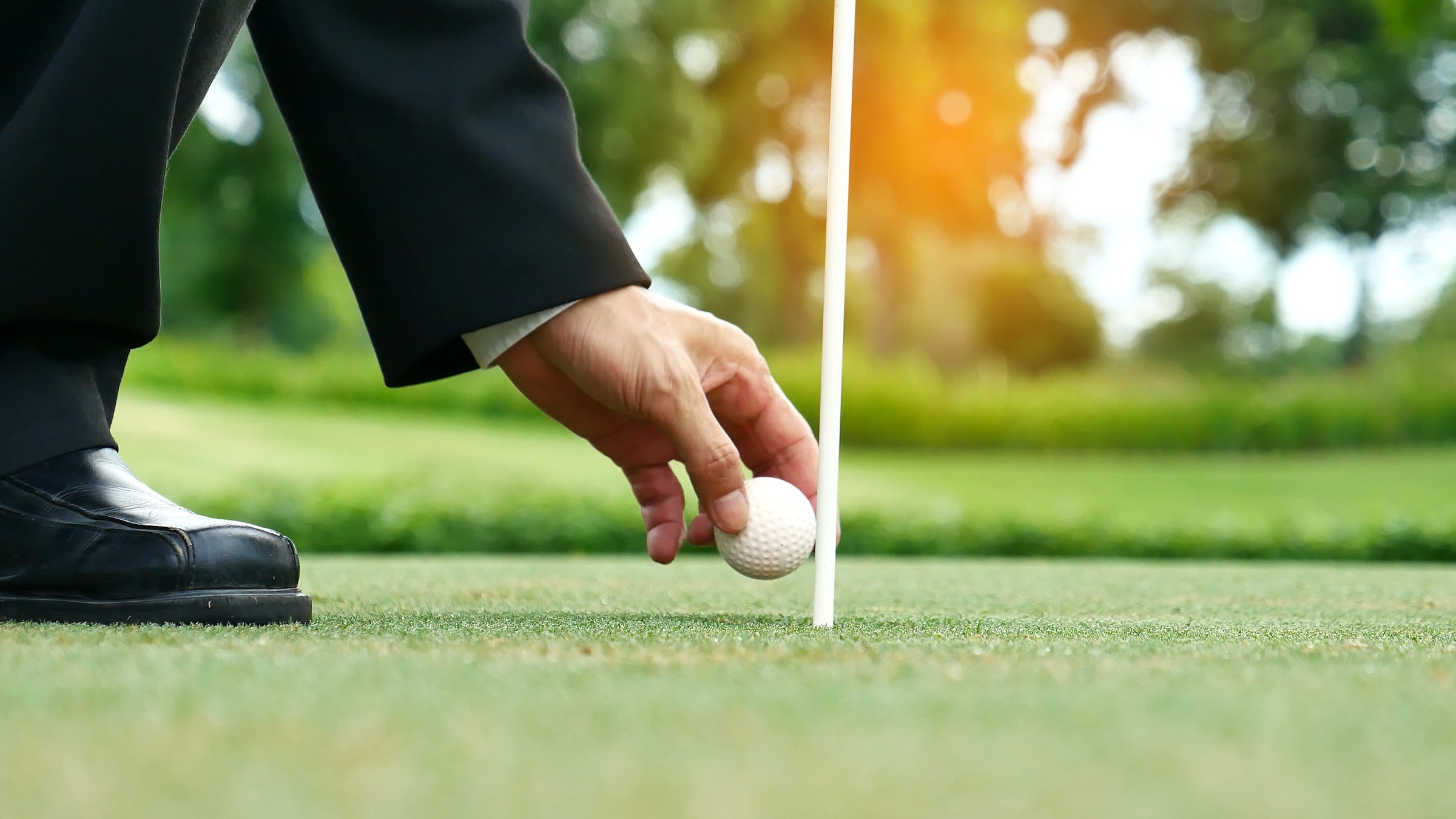 Businessman playing Golf ball practice hit swing on tee in golf club outdoor green field with recreation sport training course. Business men with black Suit driving golf Hobbies