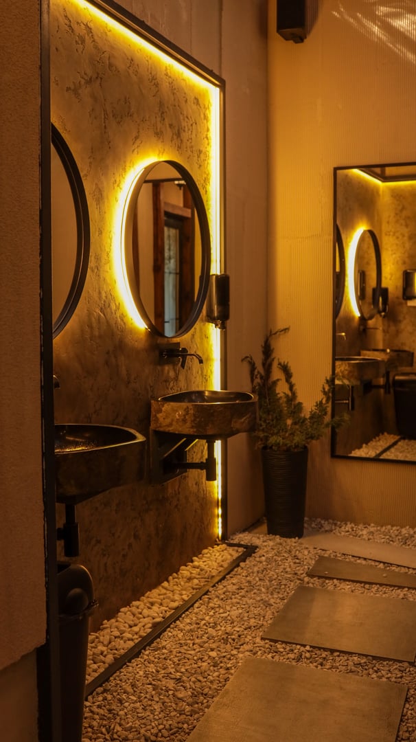 This image showcases a beautifully designed bathroom with a focus on modern aesthetics, featuring illuminated mirrors and a unique sink area. The warm lighting enhances the inviting atmosphere.