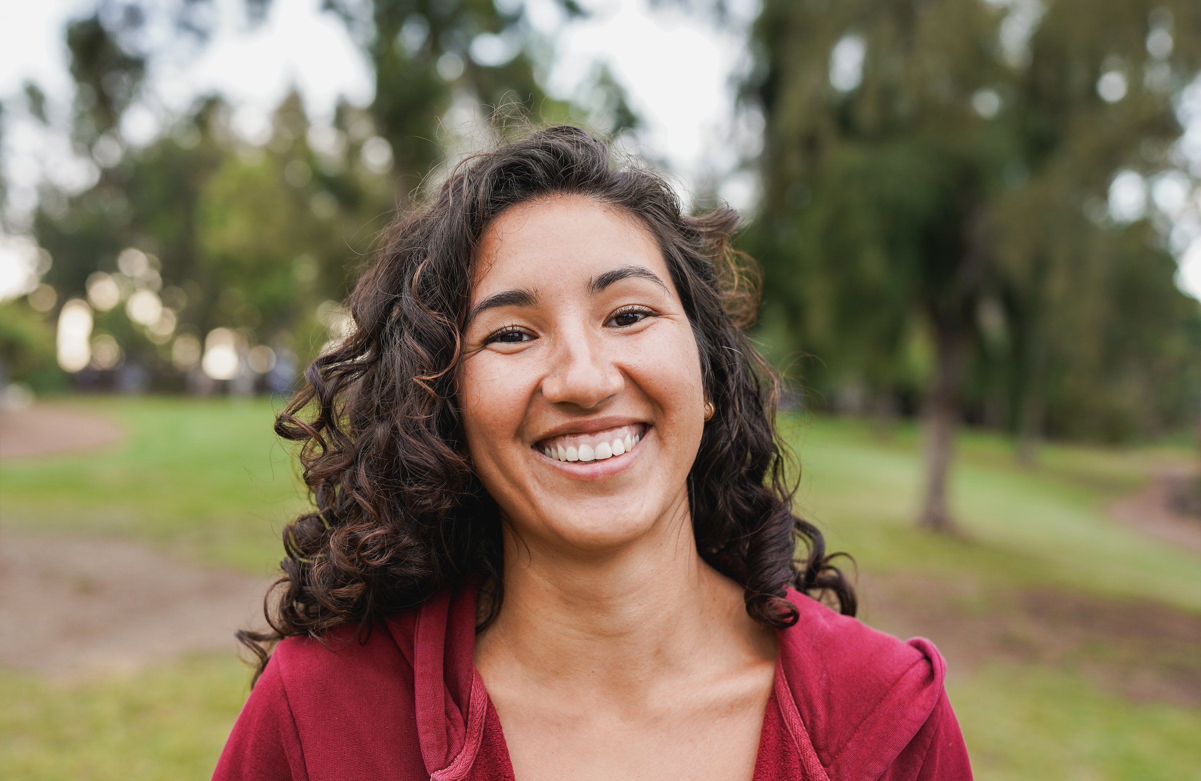 Portrait of native american woman smiling on camera with city park in background - Indigenous girl outdoor